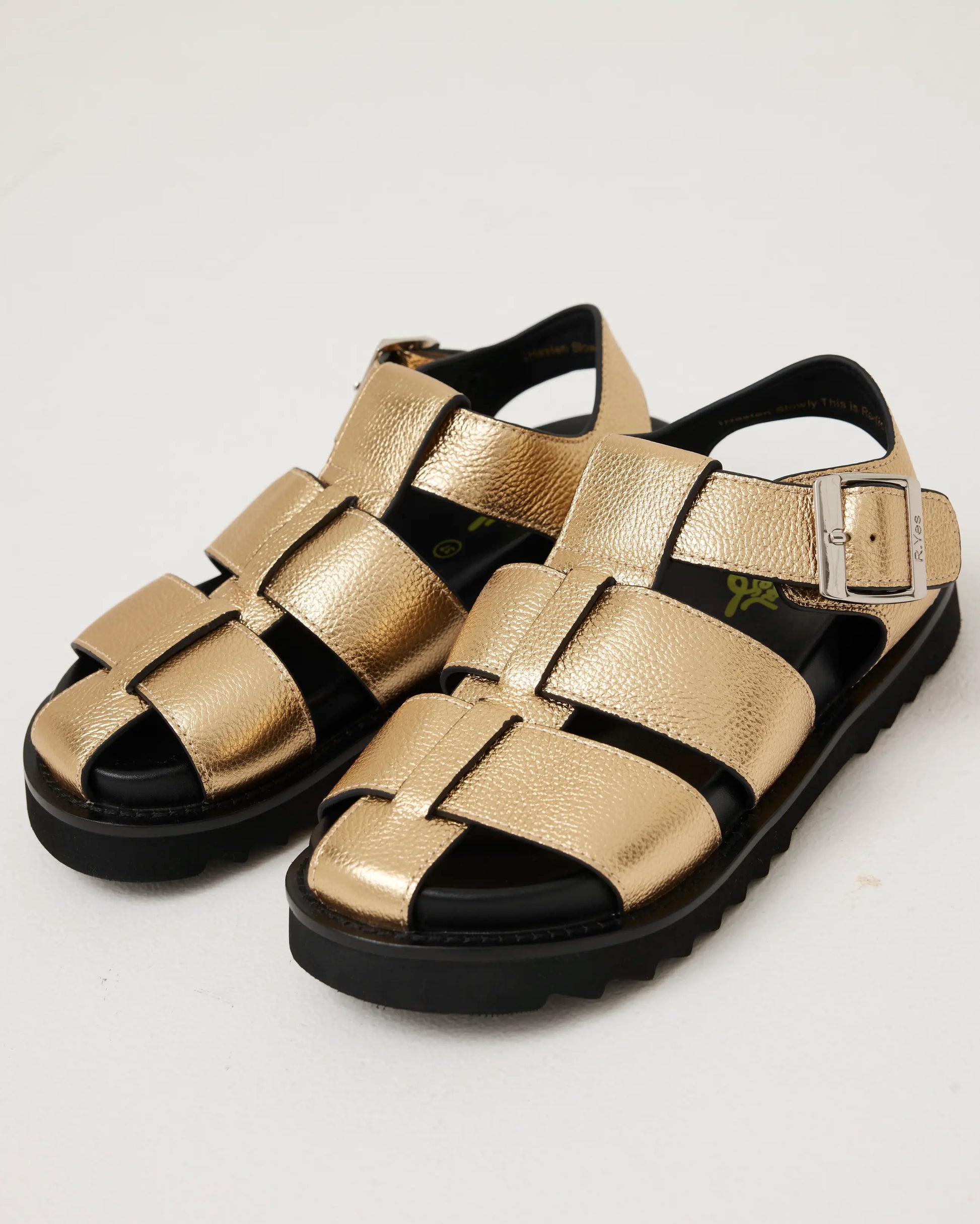 Gold metallic sandals with black soles on a white background