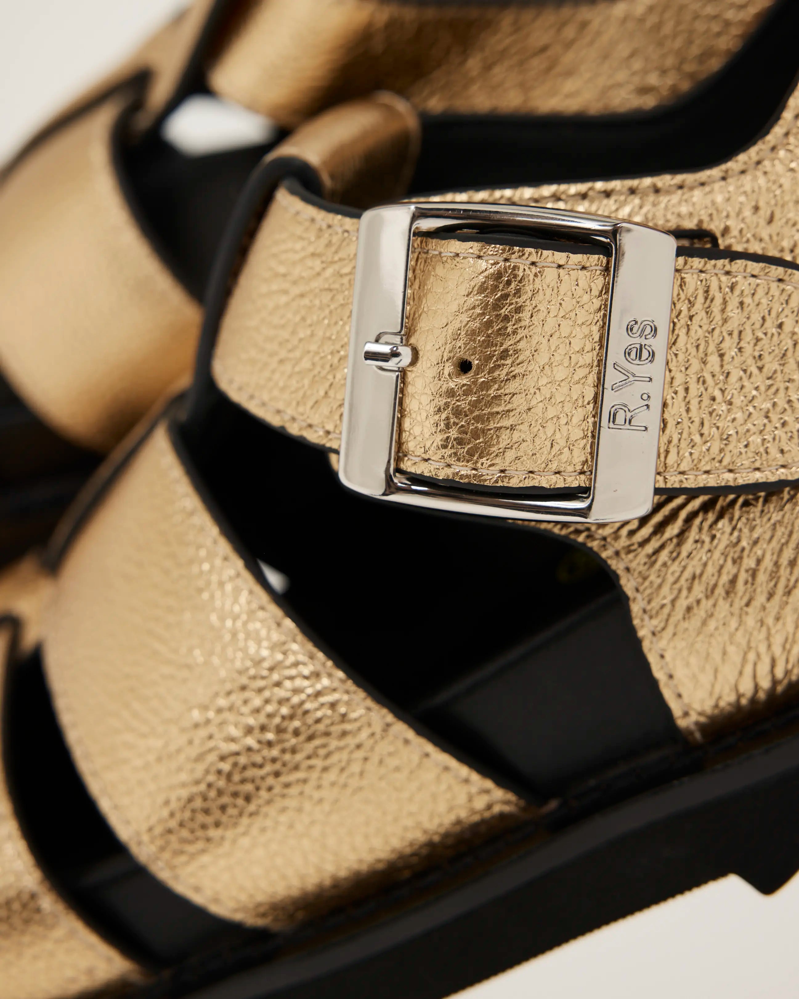 Close-up of a gold sandal with a black sole and silver buckle.