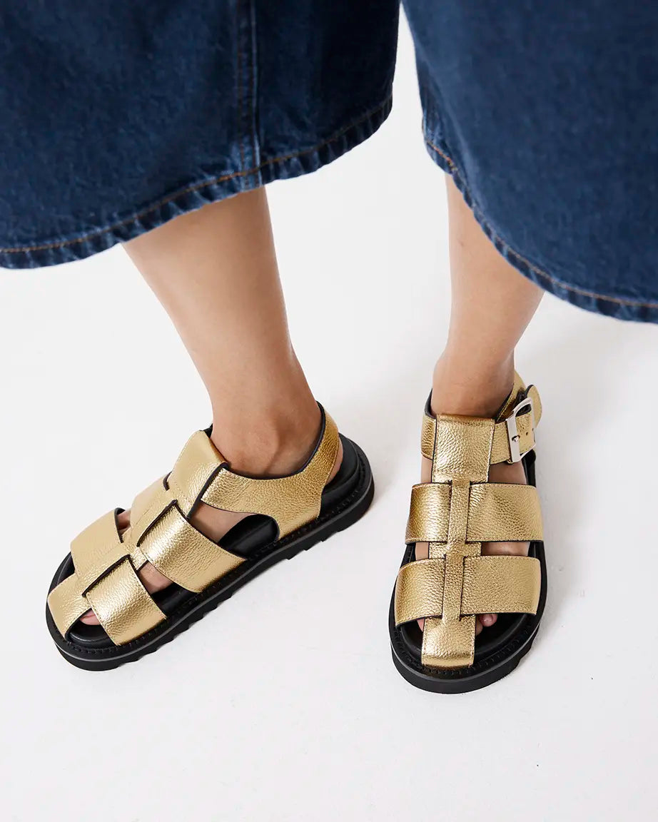 Gold fisherman sandals worn with blue jeans on a white background