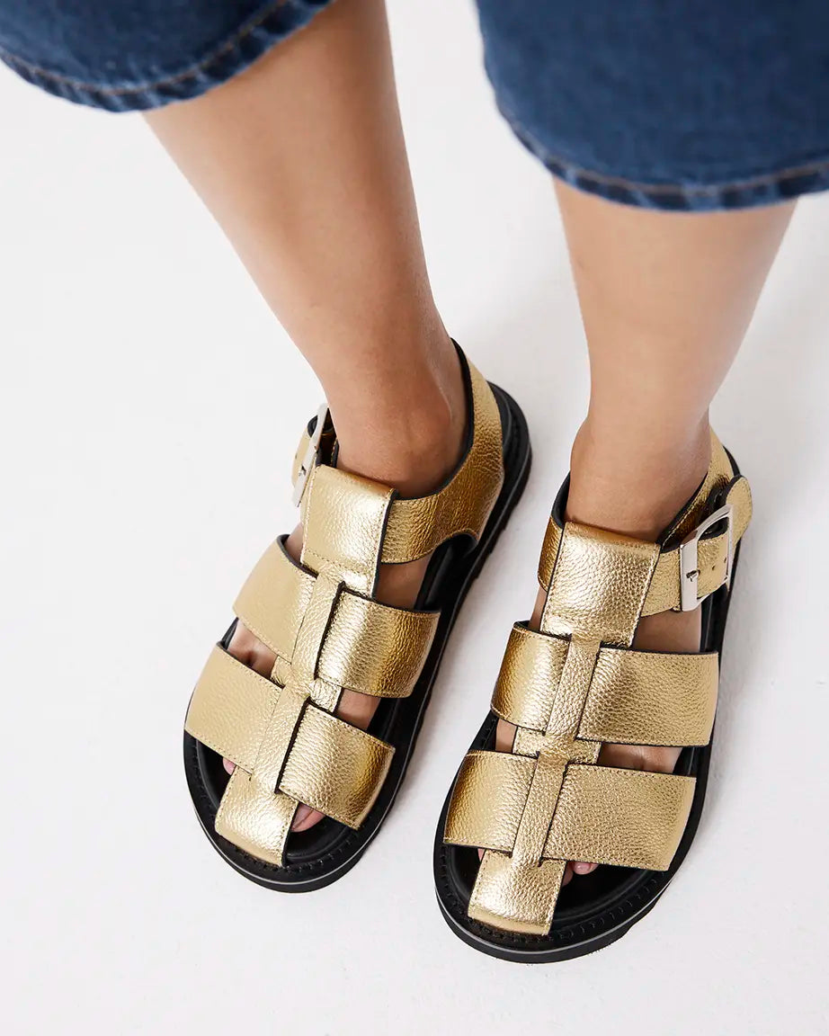 Gold fisherman sandals worn with denim shorts on a white background