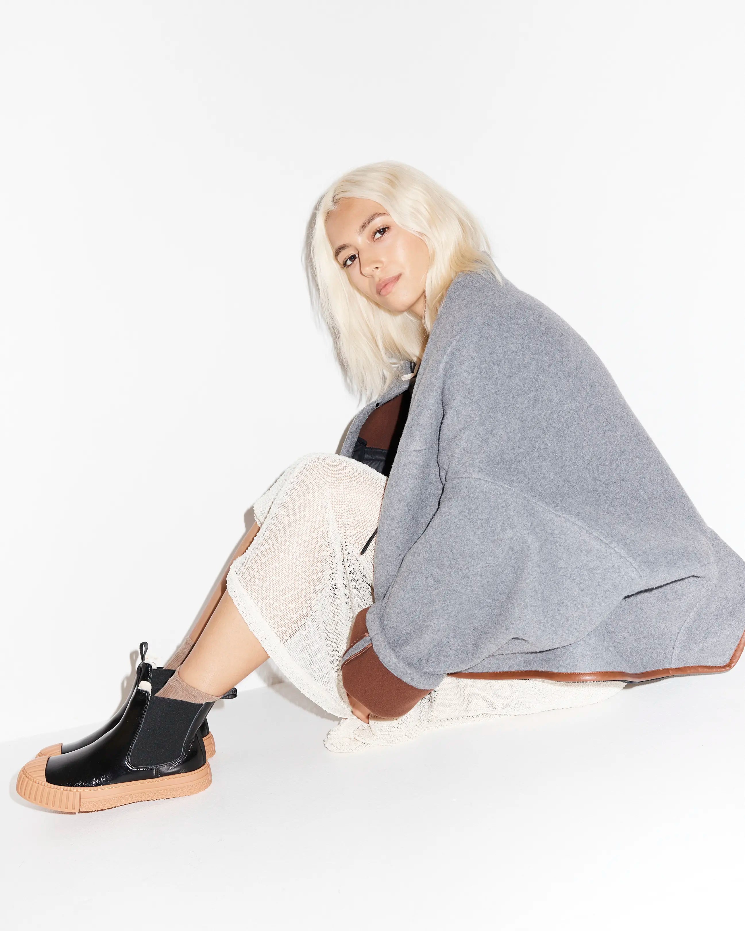 Person wearing a gray blazer, white dress and black boots on a white background