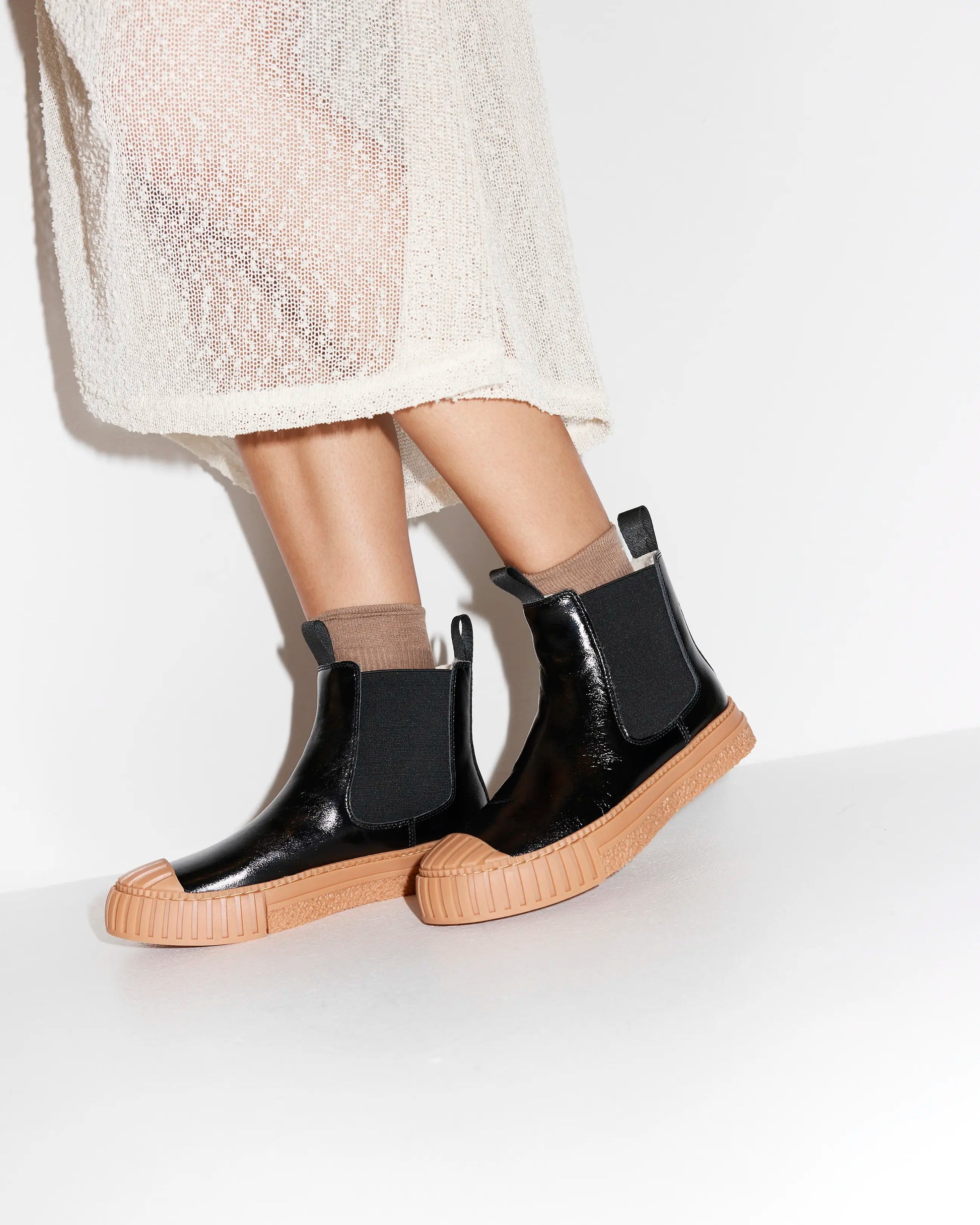 Black leather wool-lined Chelsea boot with brown sole worn with a sheer skirt