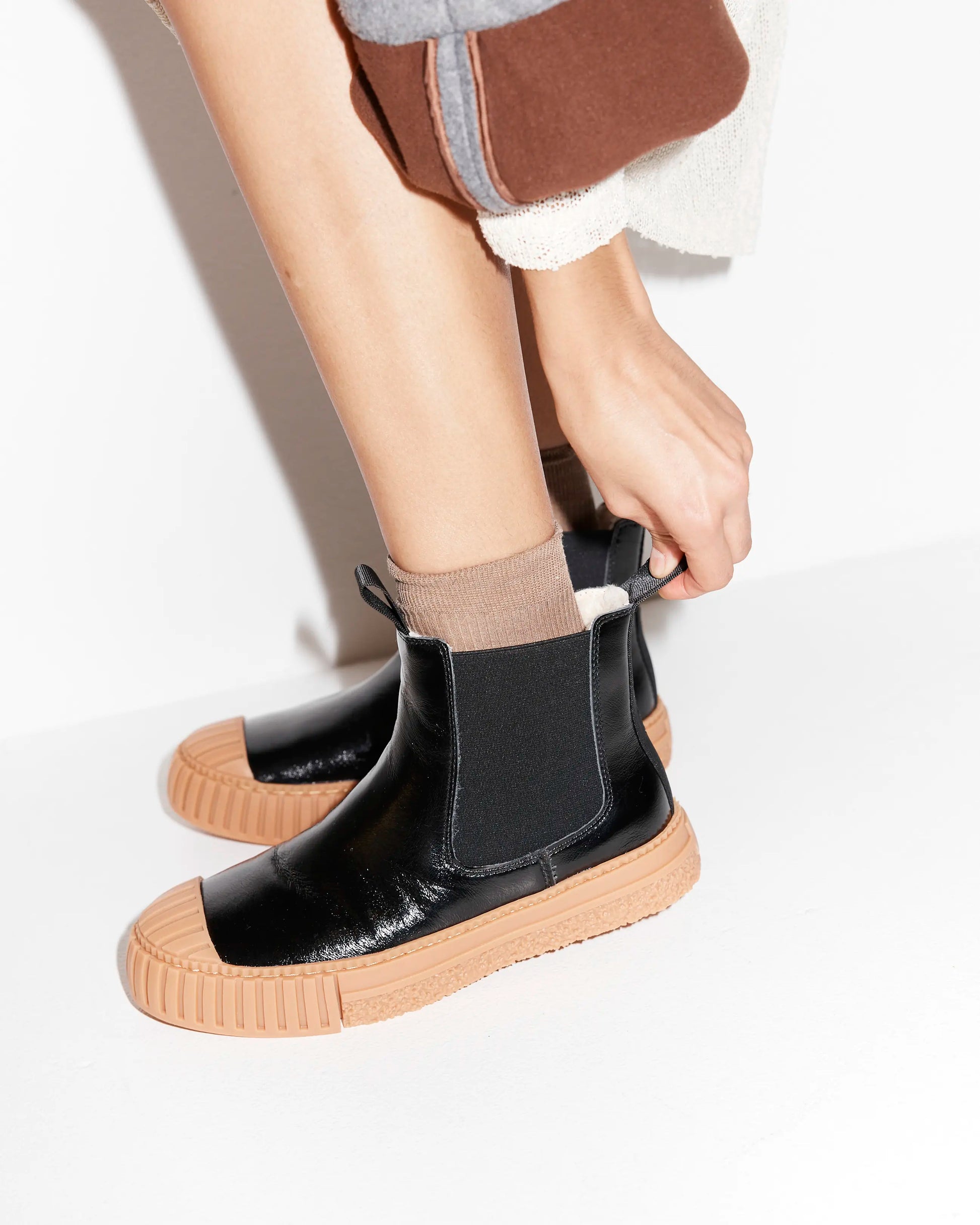 Person wearing black leather wool-lined Chelsea boots with brown soles on a white background