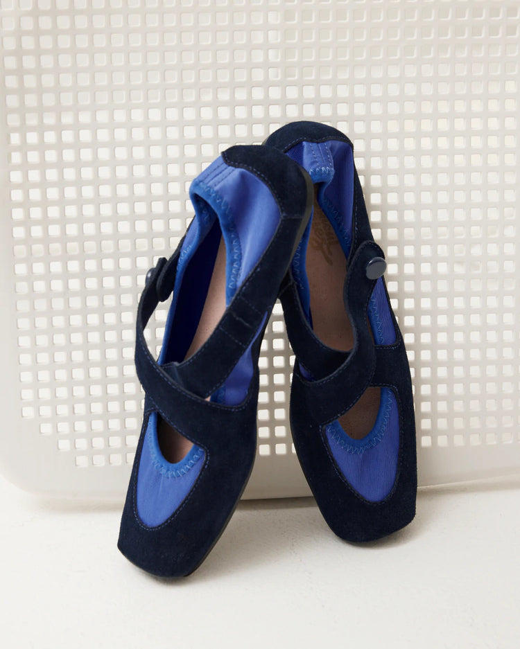 A pair of blue women's ballet flats sit propped against a white background.