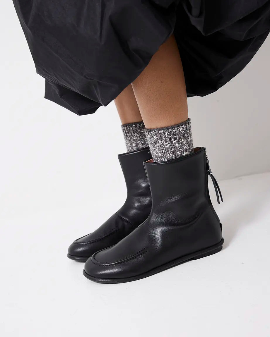 Black leather boots worn with a black skirt and sparkly socks on a white background