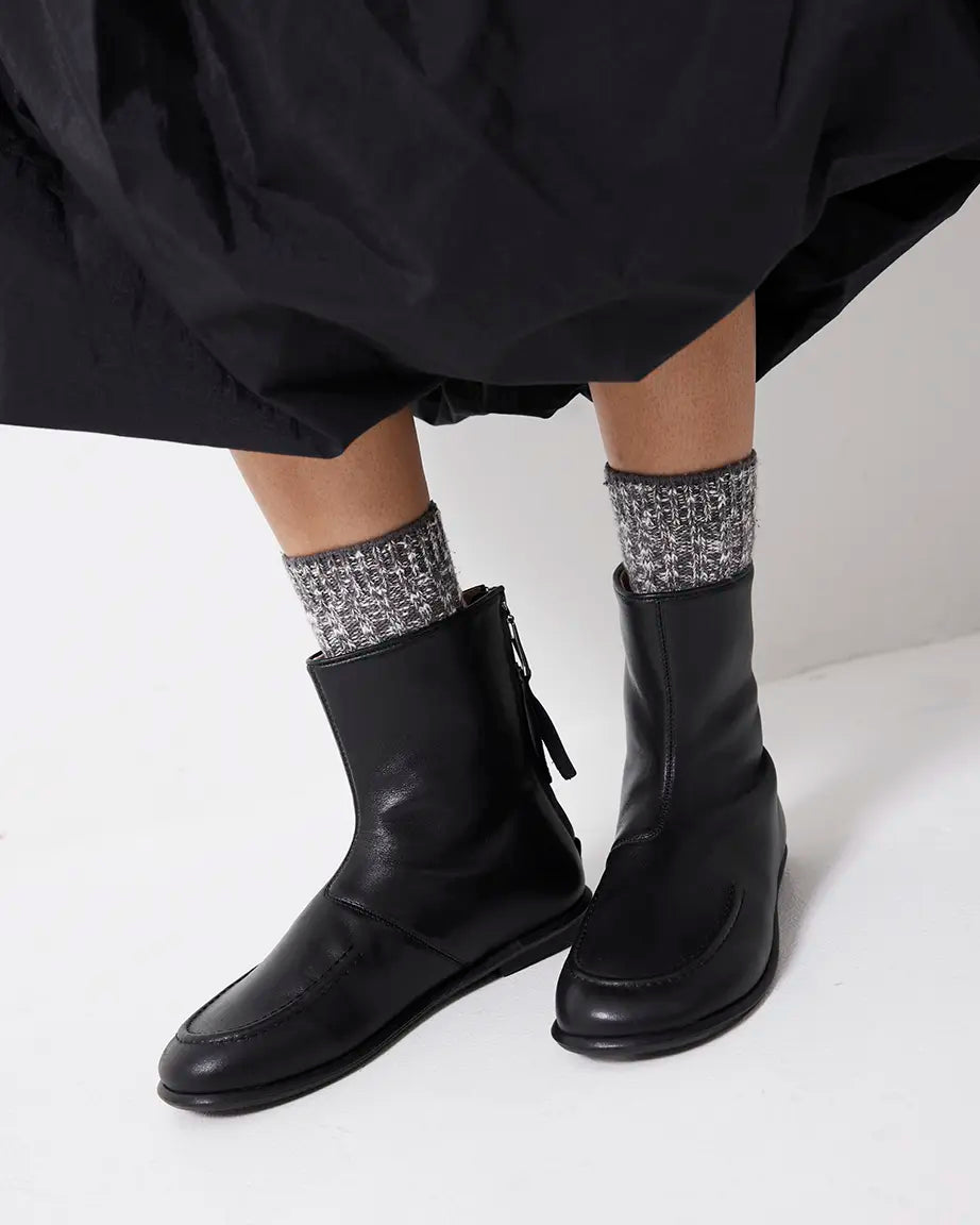 Person wearing black leather boots and patterned socks on a white background