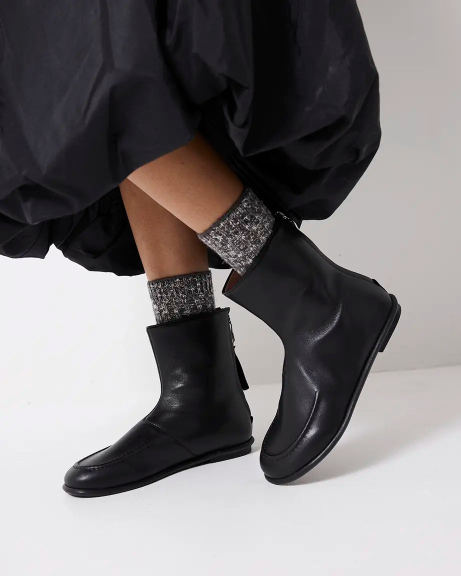 Person wearing black leather ankle boots and patterned socks on a white background
