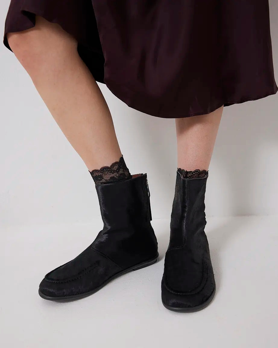 Black pony hair ankle boots worn with a dark skirt on a light background