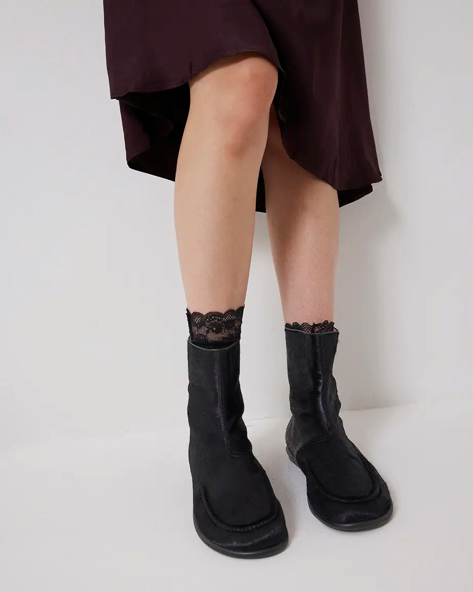 Person wearing black pony hair ankle boots and lace-trimmed socks on a plain background