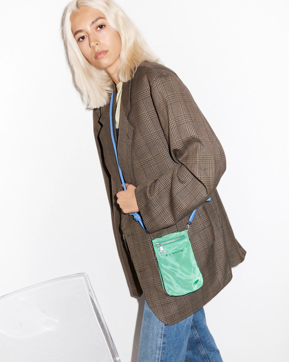 Person wearing a brown checkered coat with a bright green phone pouch and blue strap