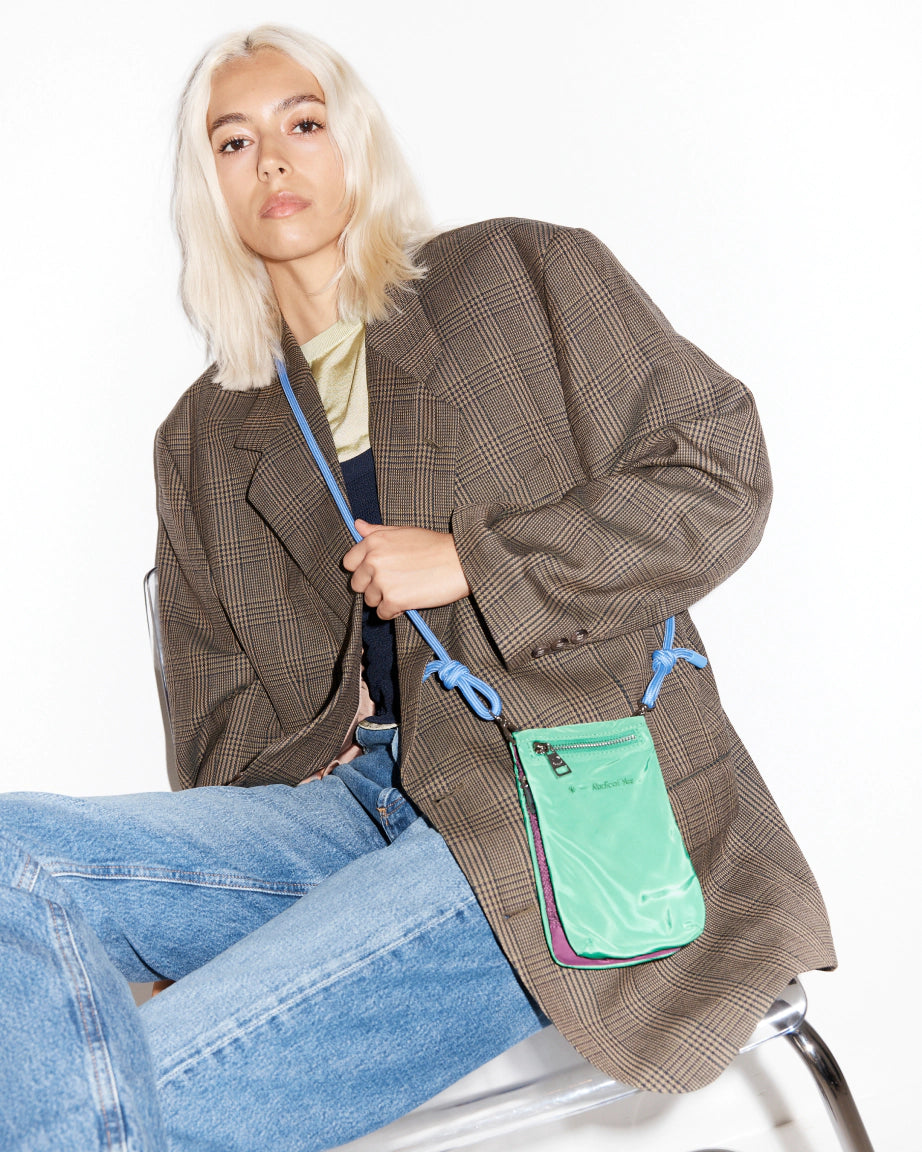 Person wearing a brown coat with a green crossbody phone pouch on a white background