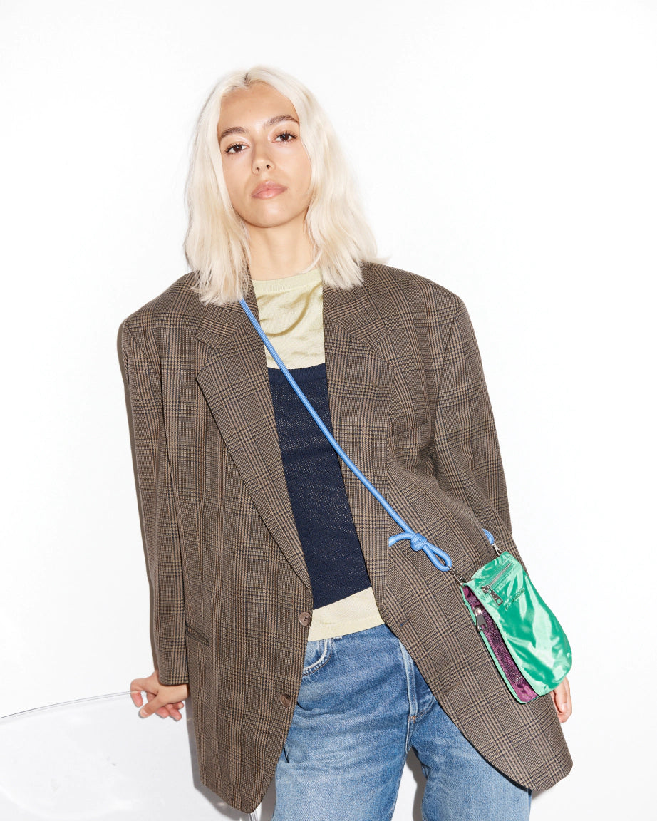 Person wearing a brown plaid blazer with a crossbody green bag on a white background