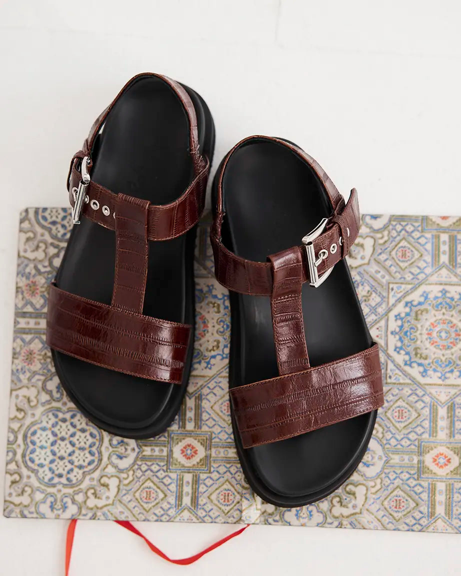 A pair of  brown leather T-bar sandals with eel-embossed detailing and black arch support soles