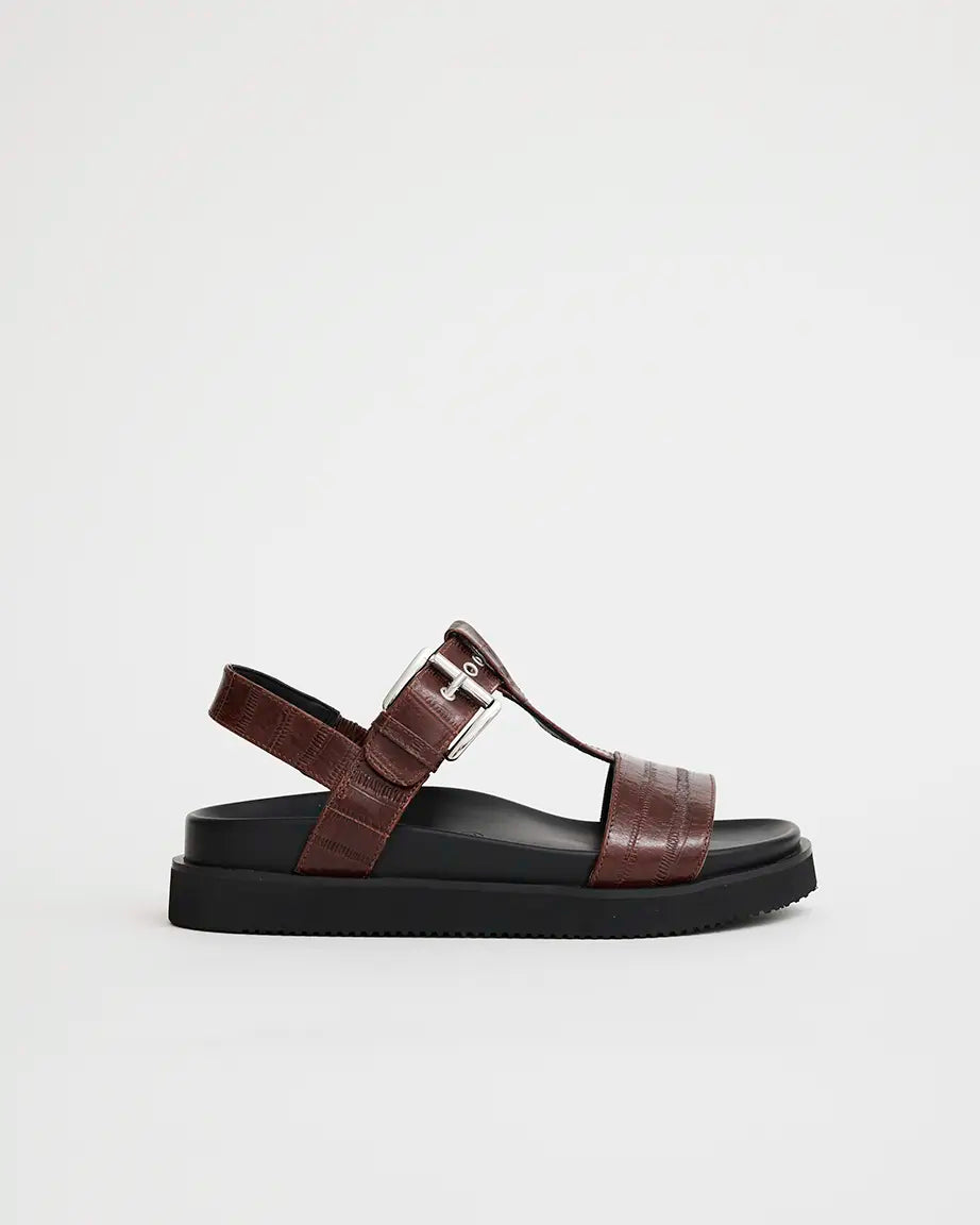 A brown leather arch support T-bar sandal with a silver buckle and black sole.