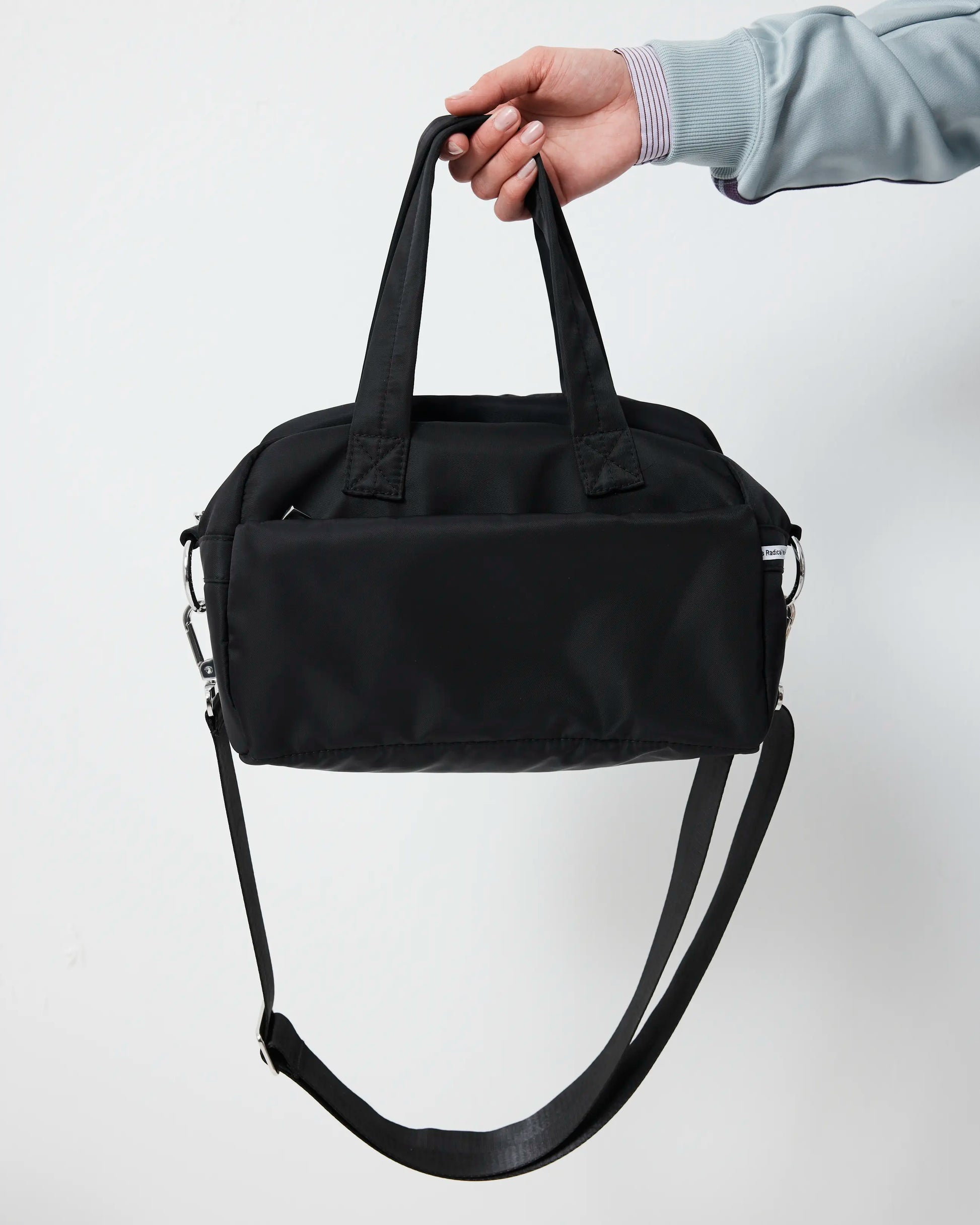 Black duffel bag held by a hand against a white background