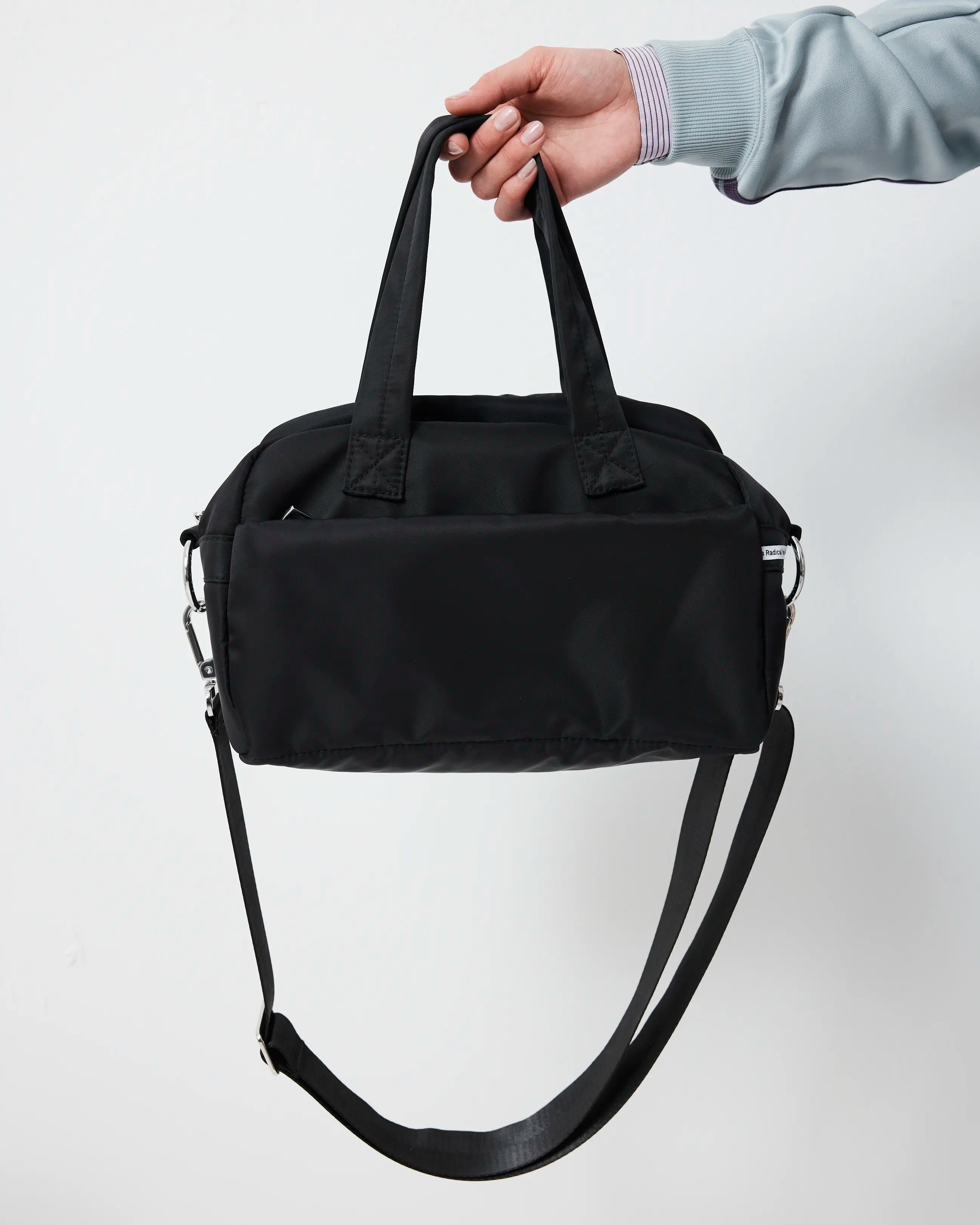 Black duffel bag held by a hand against a white background