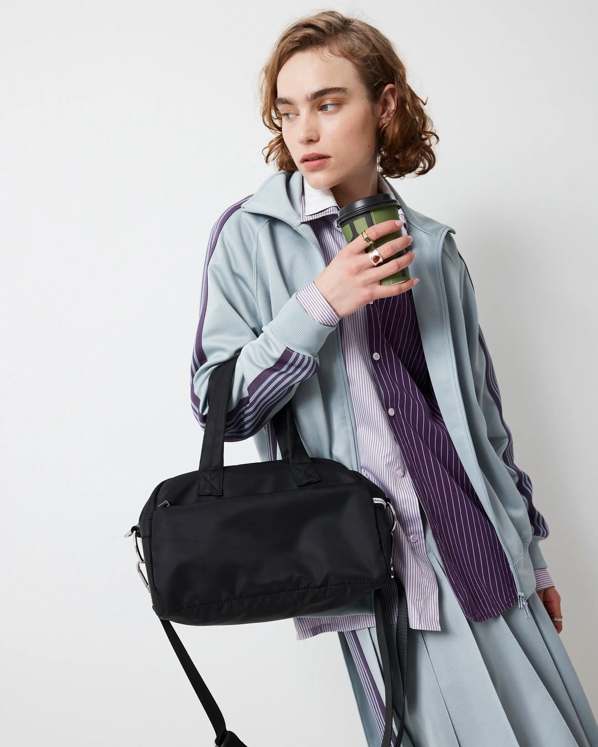 Person holding a black nylon bowling bag and a green cup