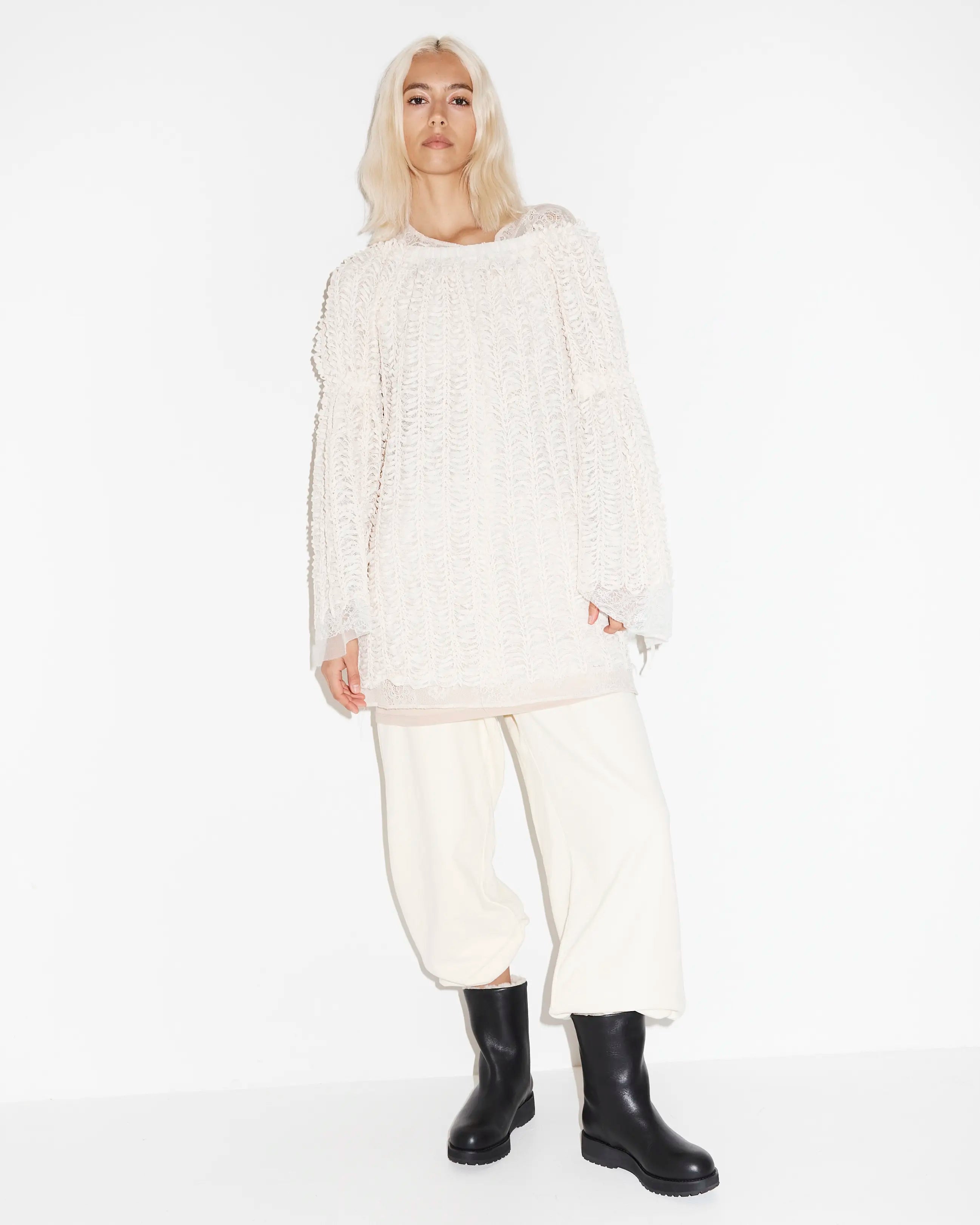 Person wearing a white outfit with black leather boots on a white background