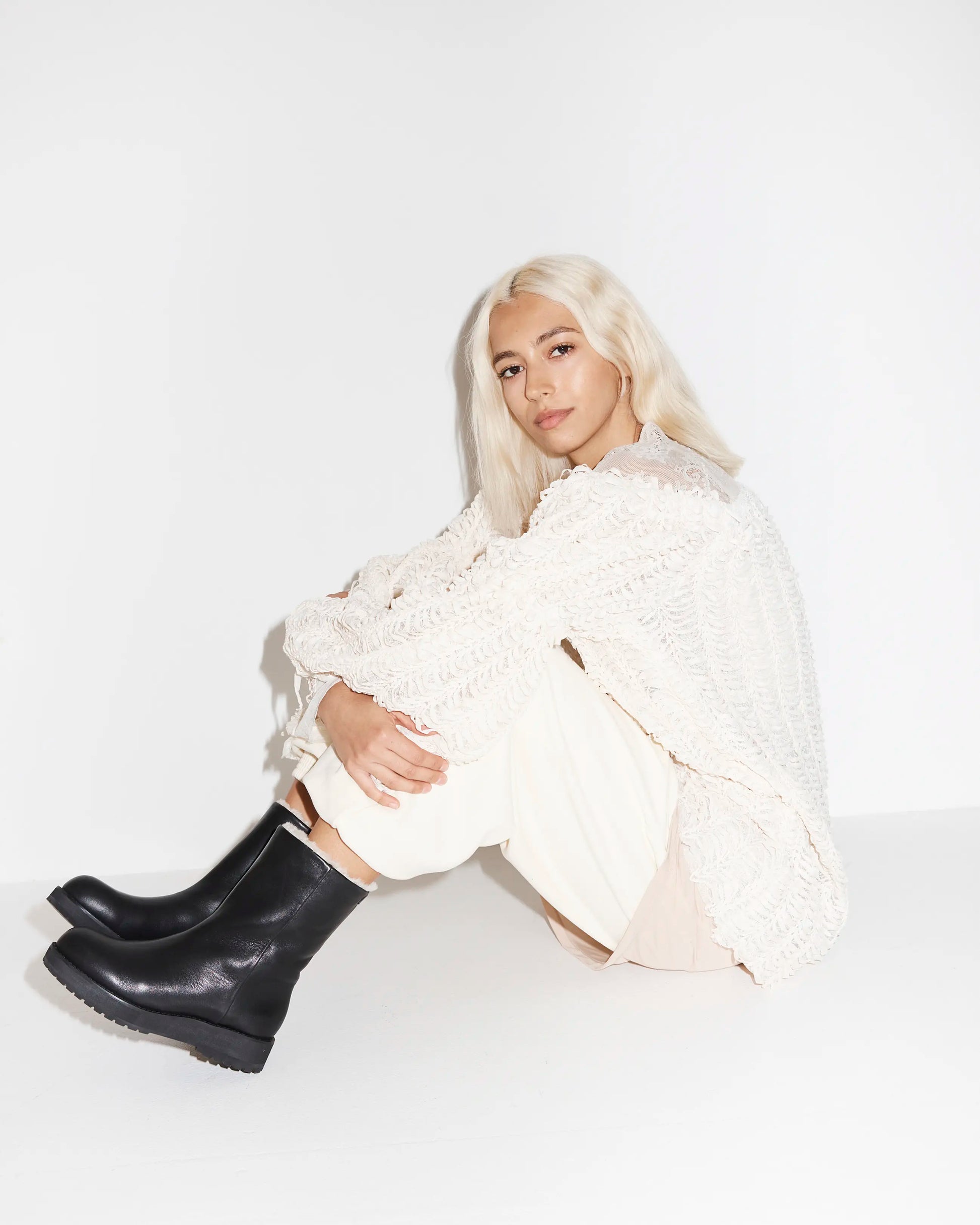 Person wearing a white outfit with black leather wool lined boots on a white background