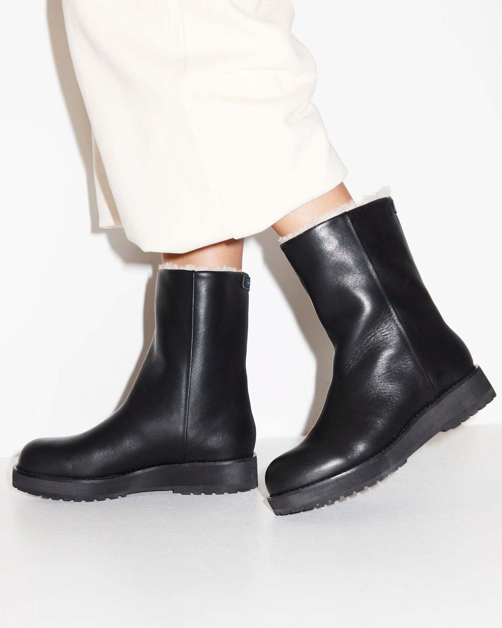 Black leather boots worn with white pants on a light background