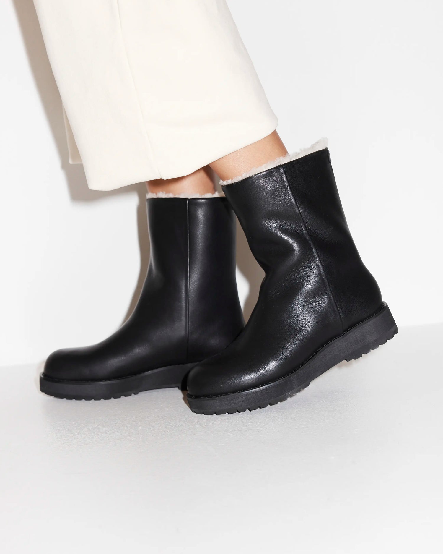 Black leather boots with wool lining worn by a person on a white background