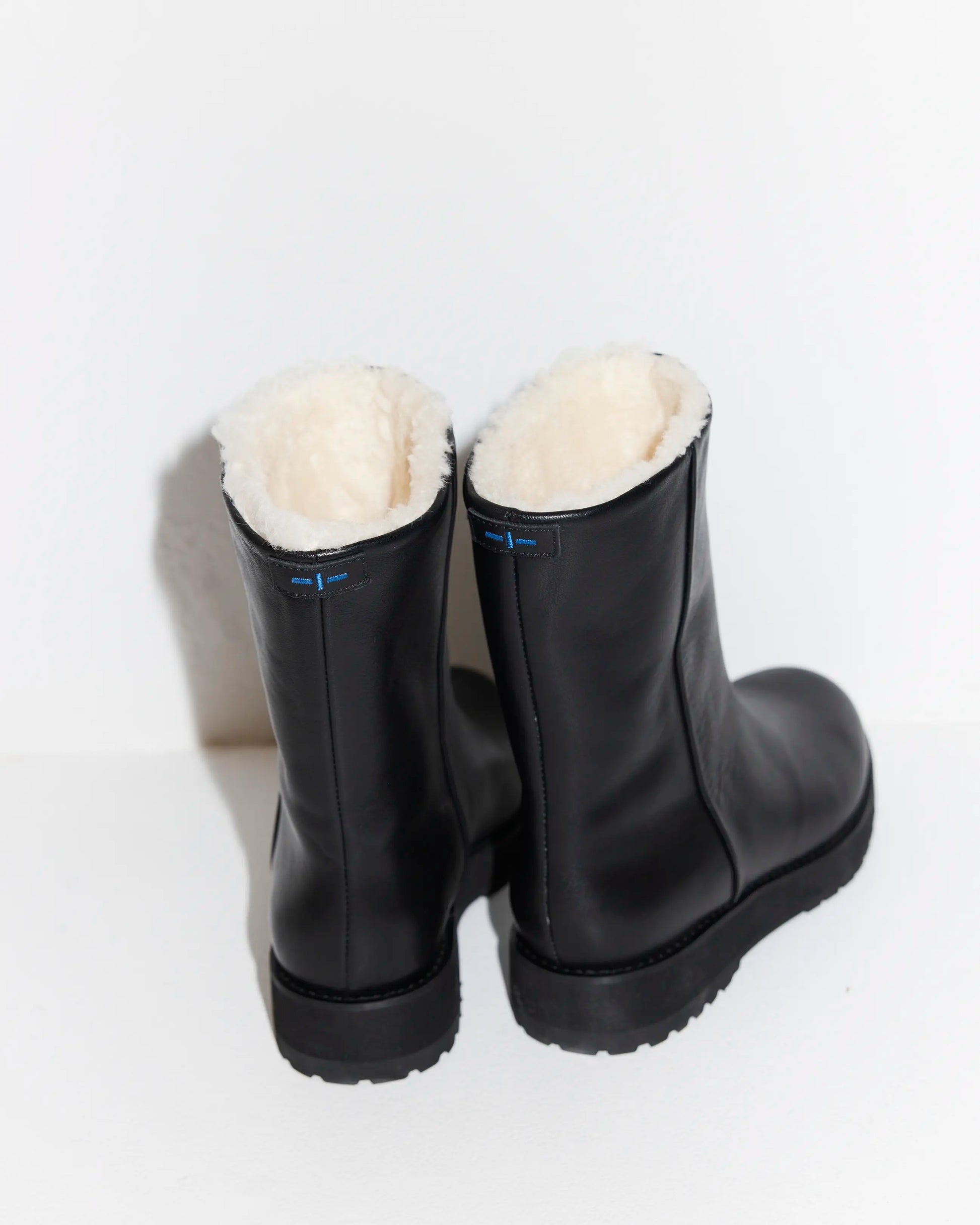 Pair of black chelsea boots with merino wool lining on a light gray background