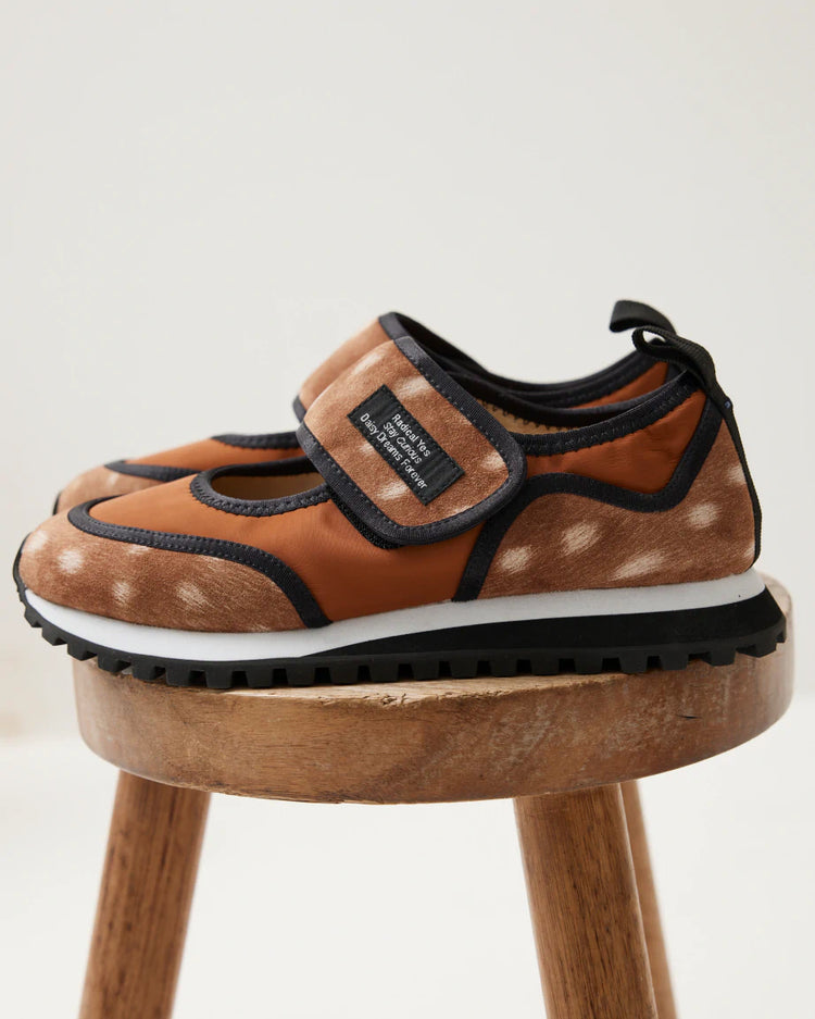 A pair of women's velcro sneakers made from material printed in a fawn pattern are placed on a wooden stool.