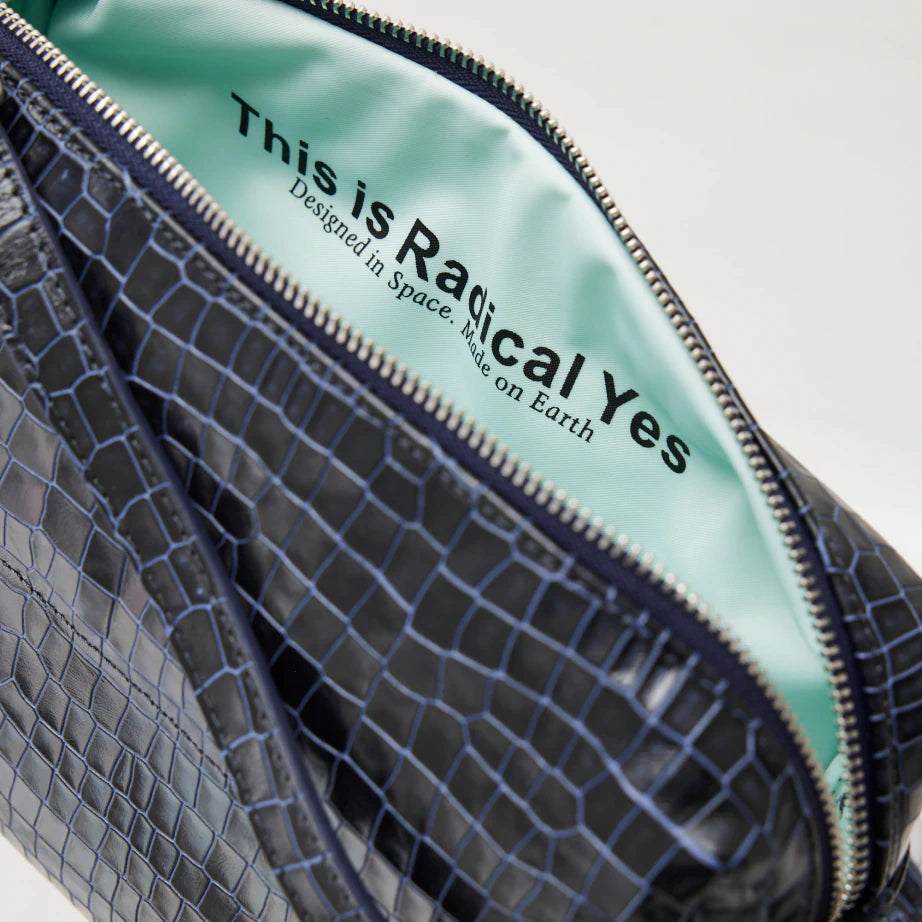 A crossbody leather bag made from blue croc leather with a thin leather strap and silver zipper and light blue lining.