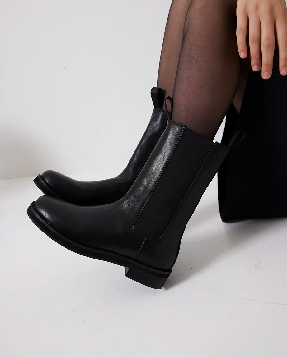 Black leather ankle boots worn with sheer black tights on a white background