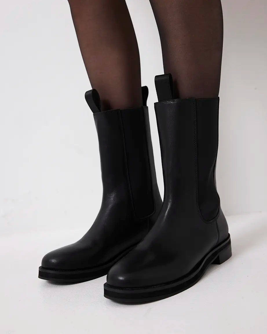 Black leather riding boots worn with tights on a white background