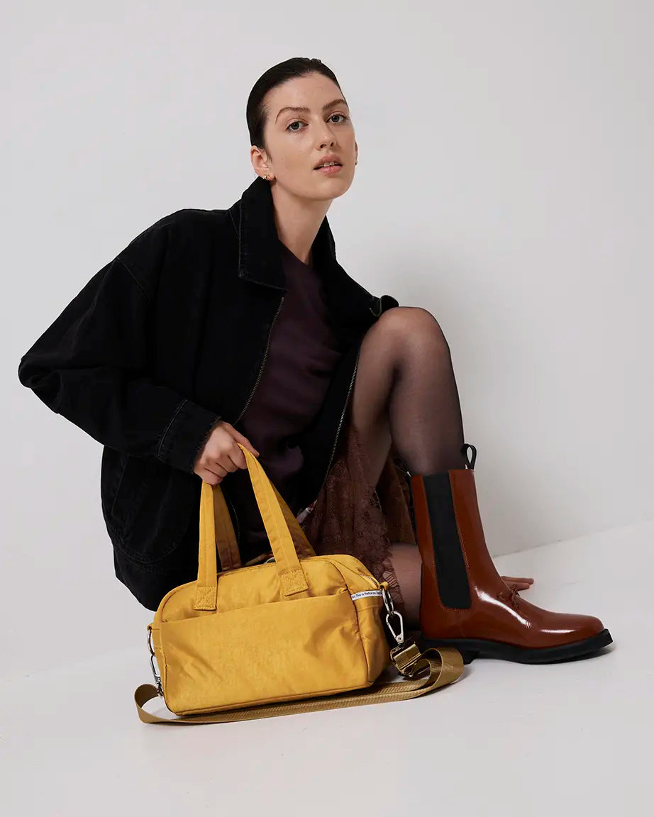 Person holding a yellow bag with brown boots on a white background