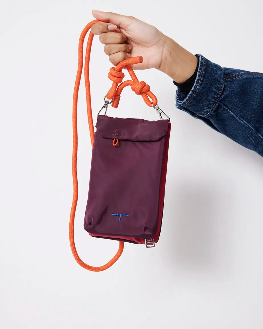 Purple pouch with orange strap held by a hand on a white background