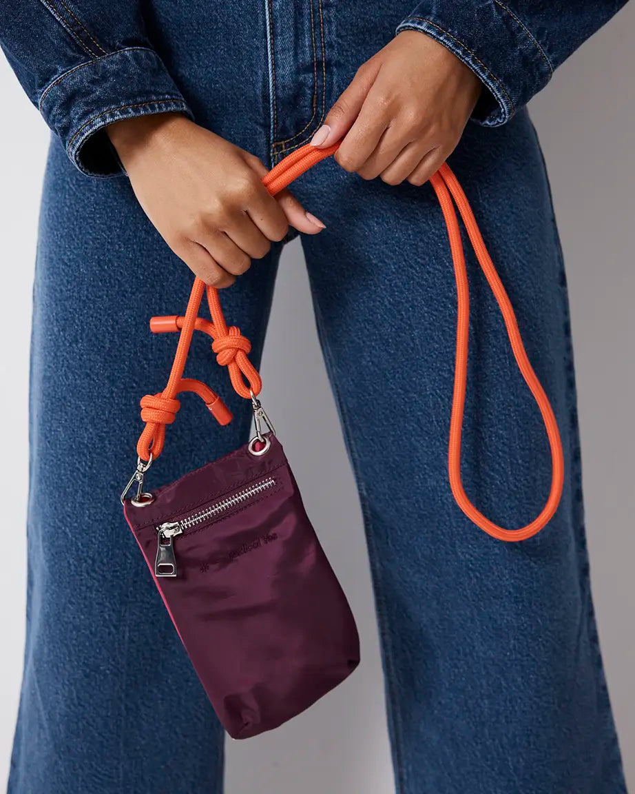 Person holding a purple pouch with an orange strap against a gray background