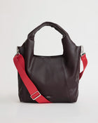 Purple leather handbag with a red strap on a light gray background