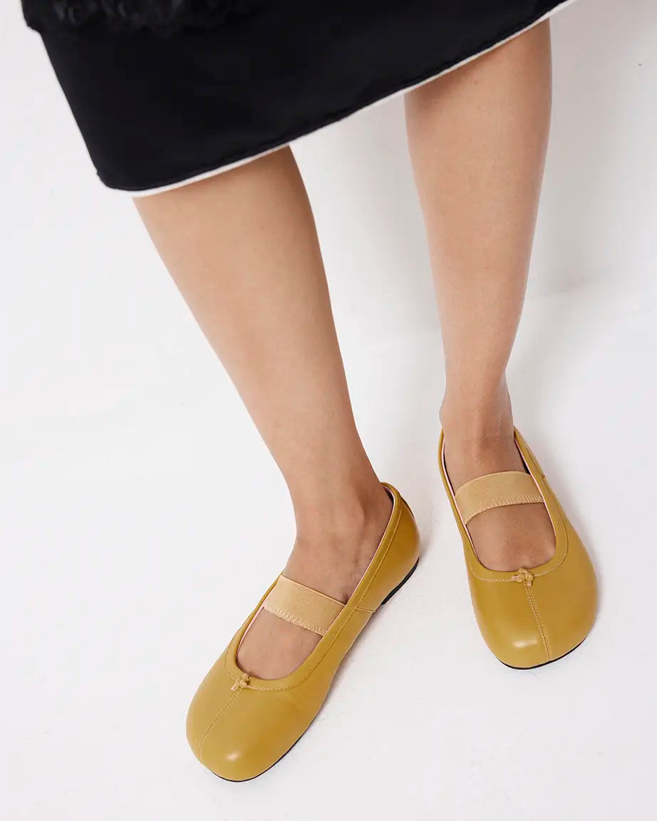 Yellow flat shoes worn with a black skirt on a white background