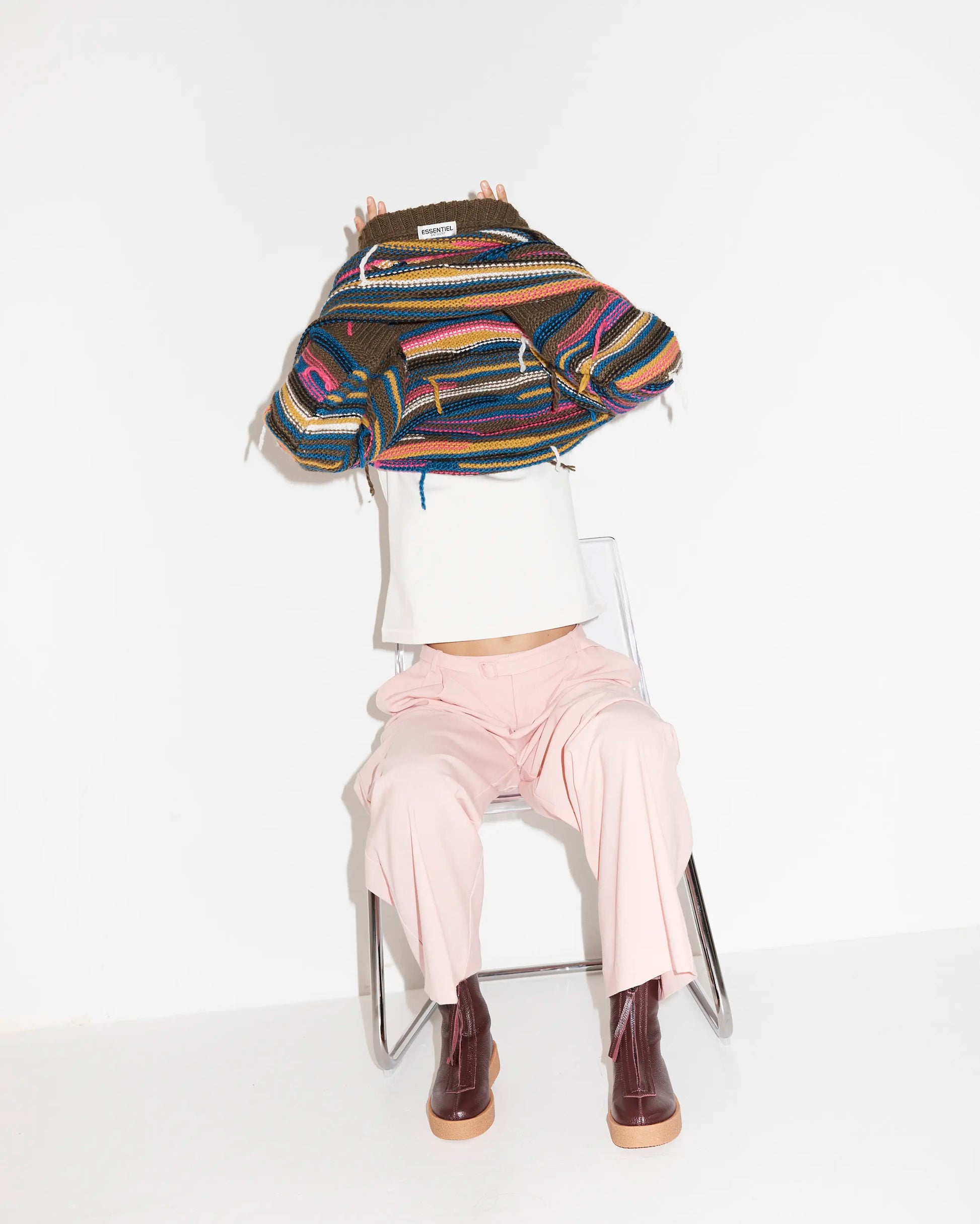 Person wearing a colourful striped sweater and purple boots sitting on a chair