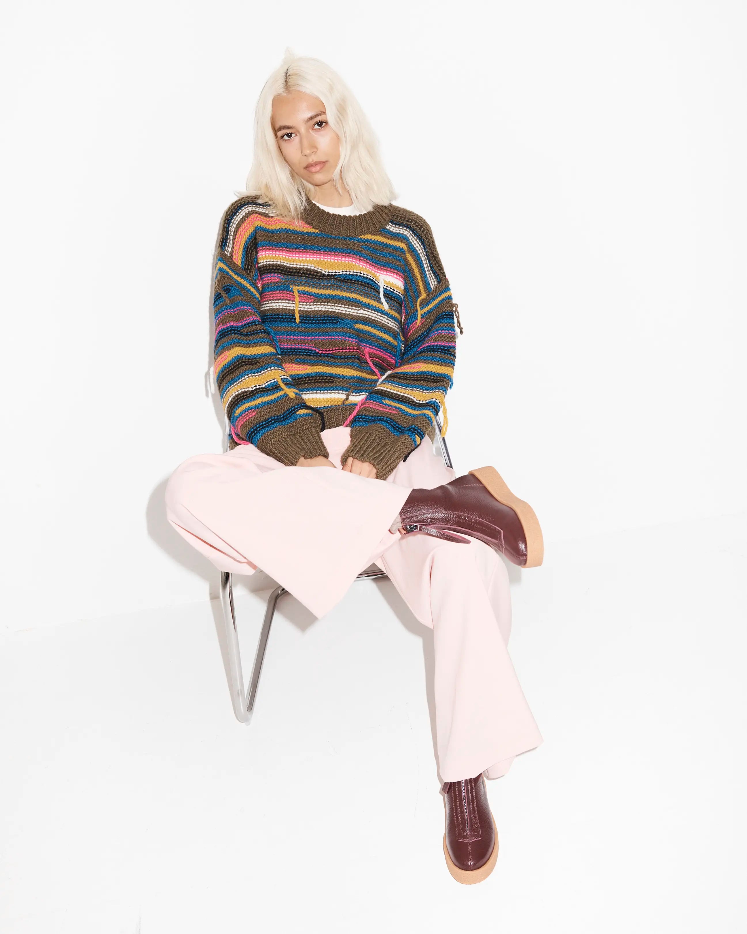 Person wearing a colourful striped sweater and purple boots sitting on a chair