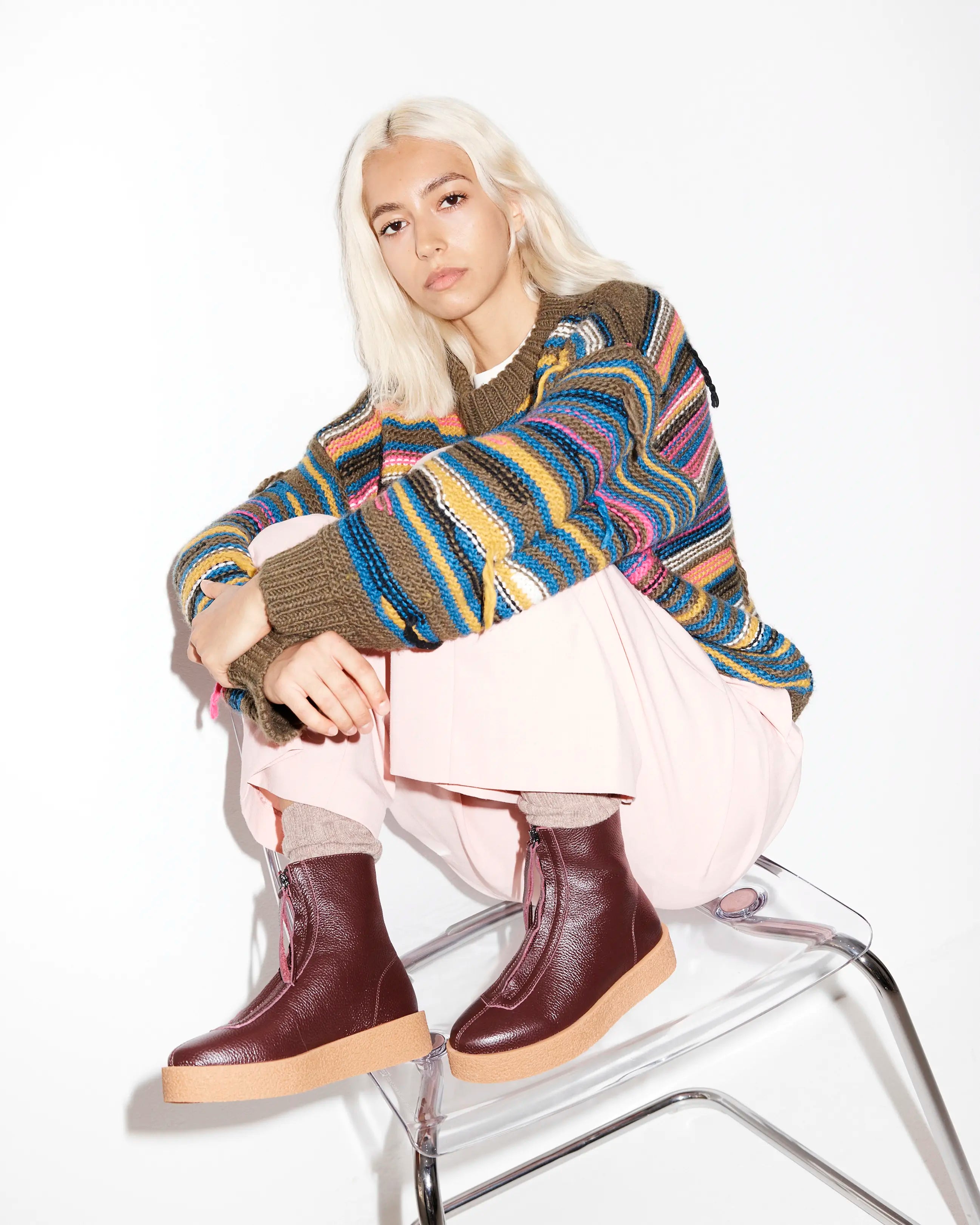 Person wearing a colourful sweater and purple boots sitting on a chair.
