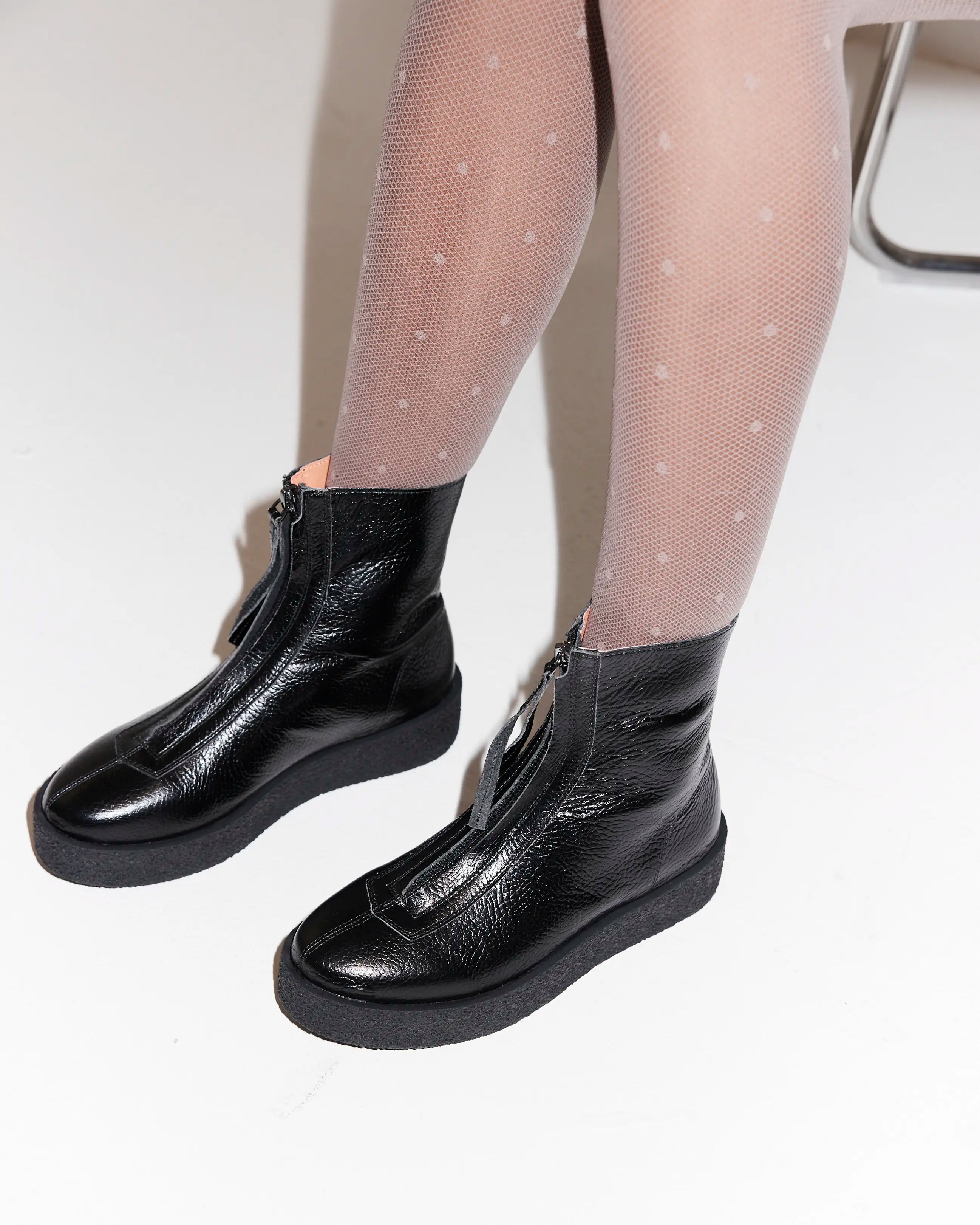 Black leather ankle boots worn with polka dot tights on a light background