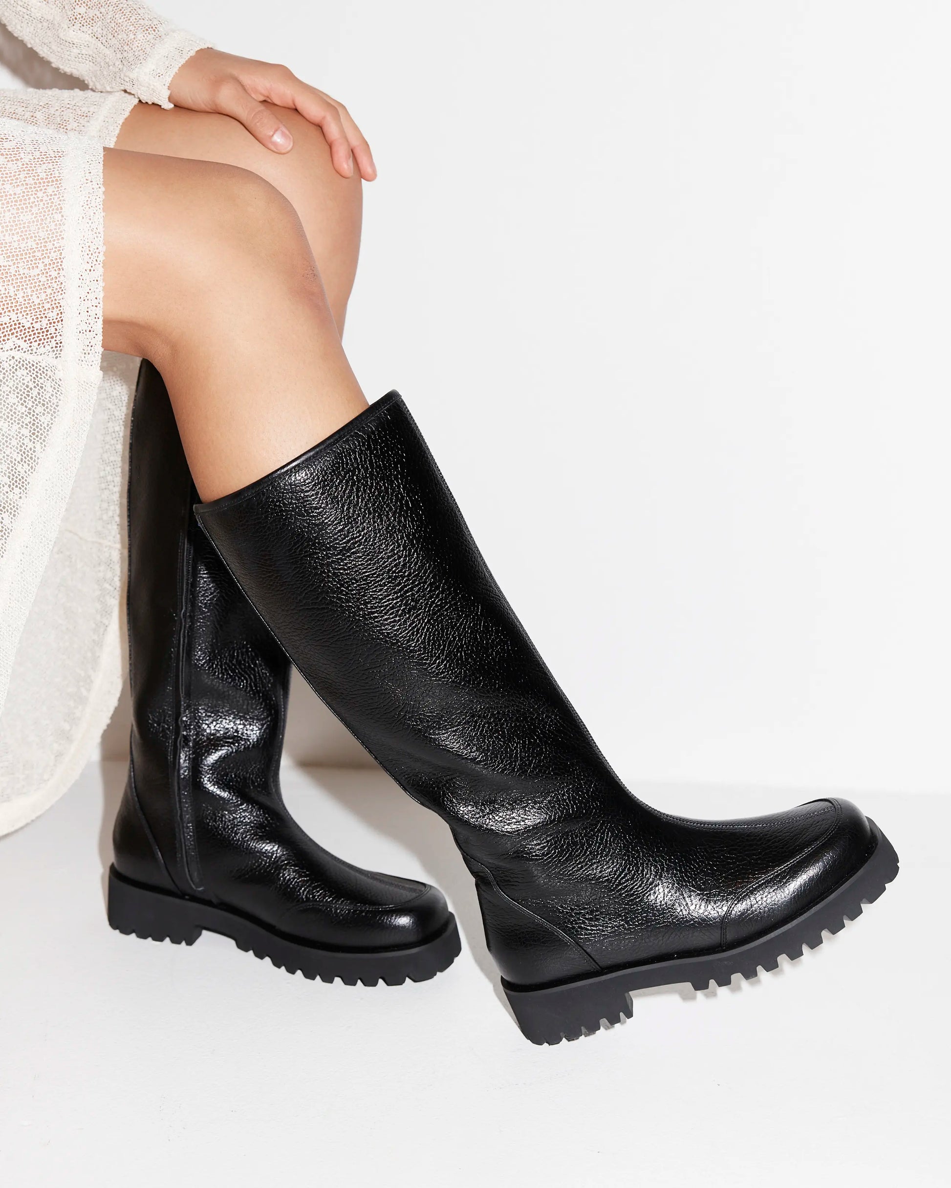 Black leather knee high boots worn by a person on a white background