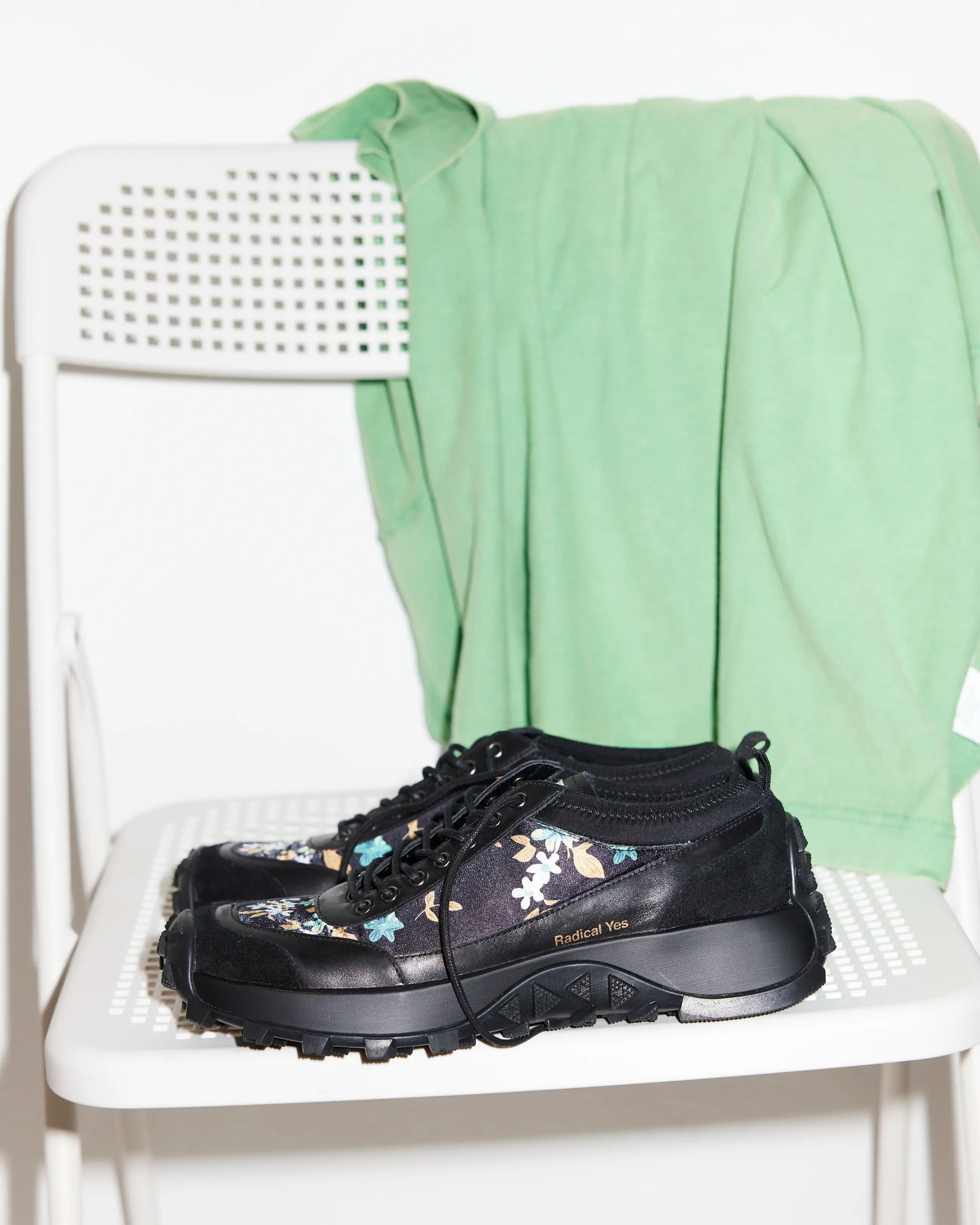 Black floral-patterned shoes on a white chair with a green garment draped over it