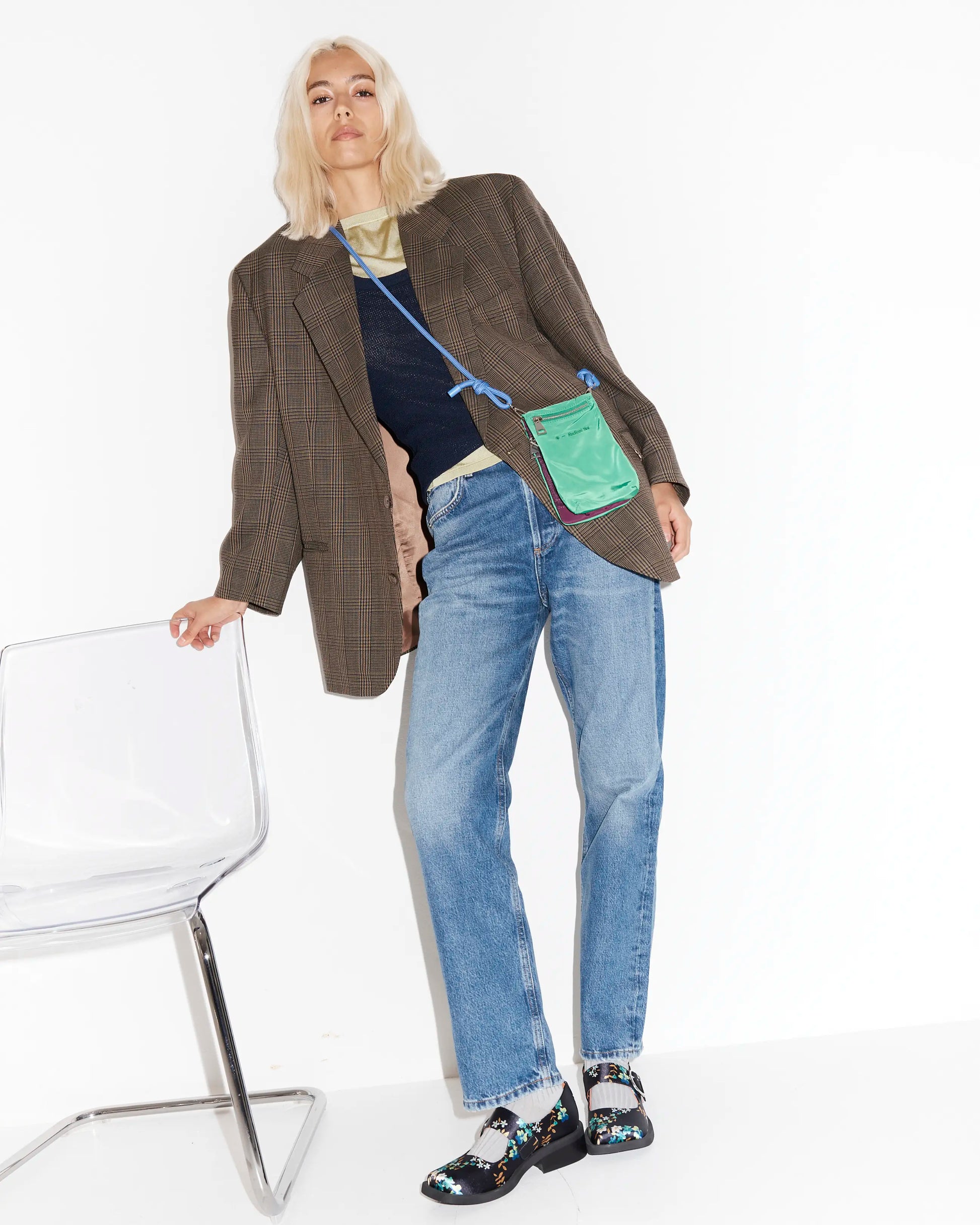 Person wearing a brown blazer with floral square toe shoes and a bright green pouch