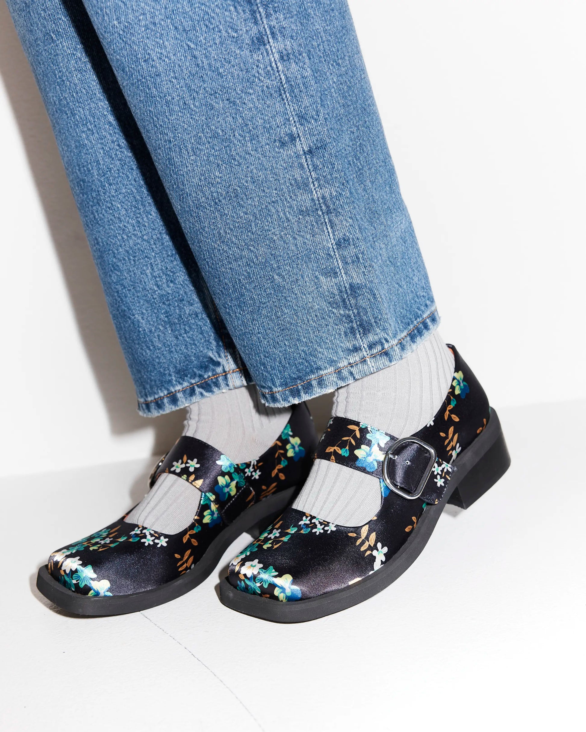 Navy floral square toe shoes worn with blue jeans and white socks on a light background