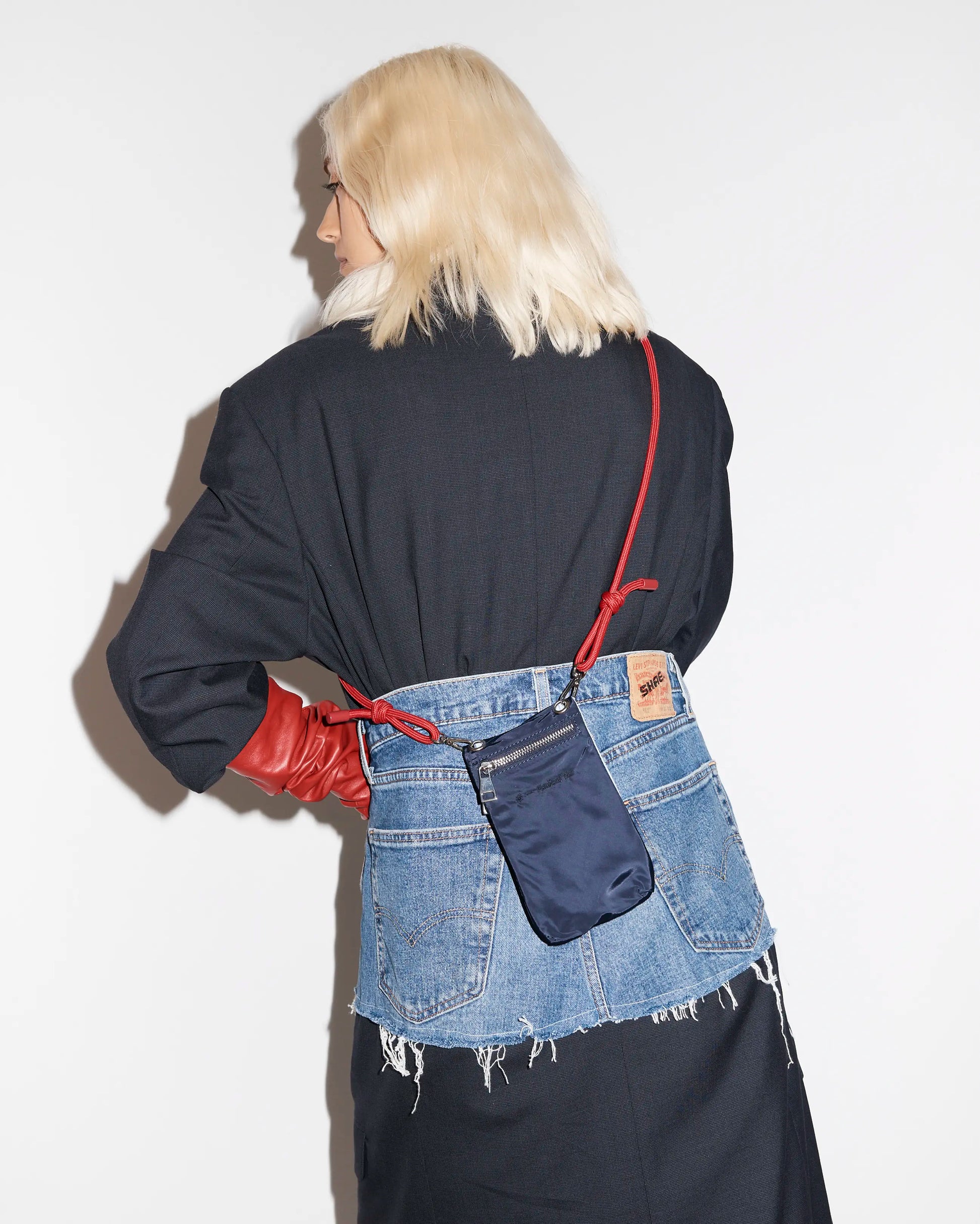 Person wearing a denim skirt carrying a navy phone pouch with a red strap