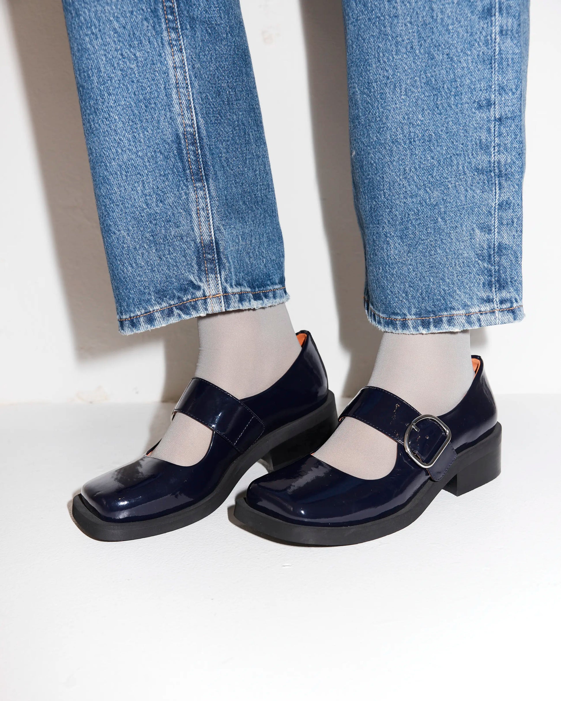 Navy blue leather square toe shoes worn with light blue jeans on a white background