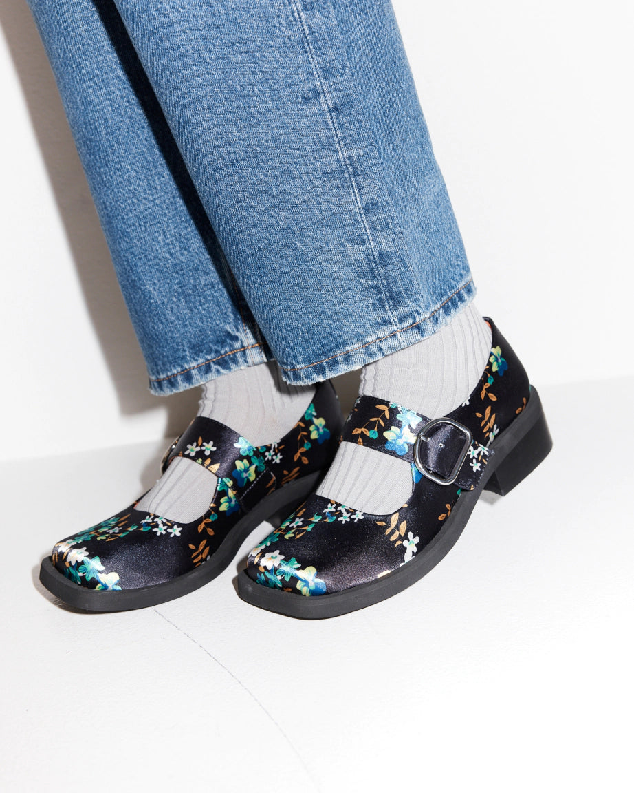 Navy floral square toe shoes worn with blue jeans and white socks on a light background