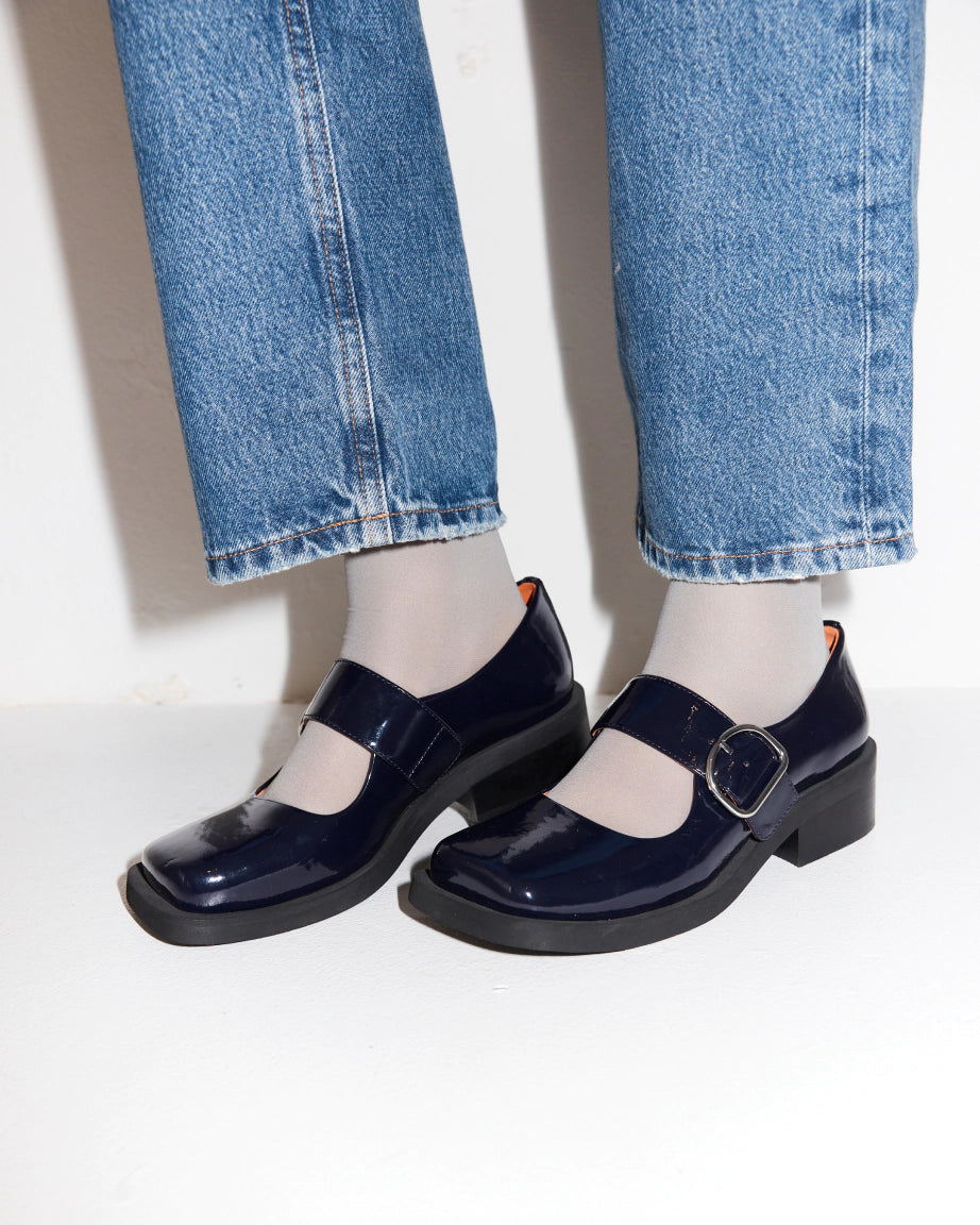 Navy blue leather square toe shoes worn with light blue jeans on a white background