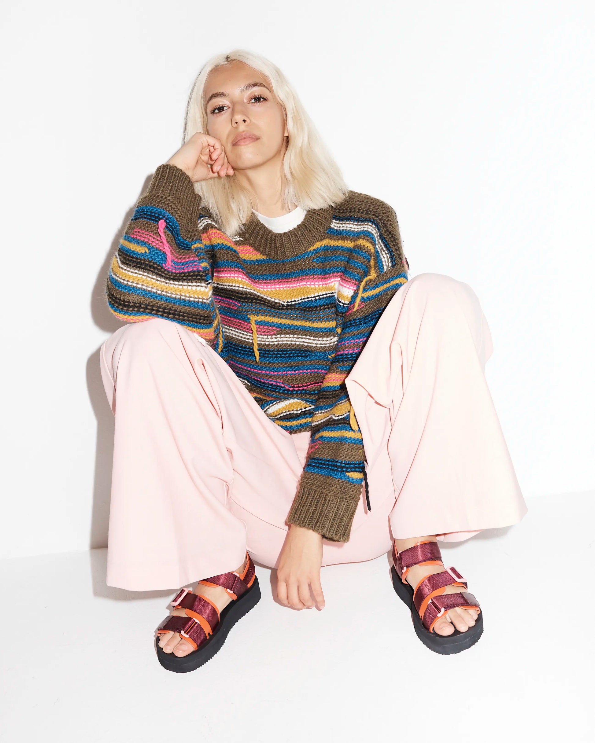 Person wearing a colorful striped sweater and athletic sandals on a white background