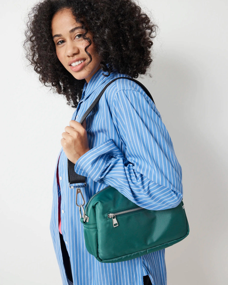 Woman wearing a blue striped shirt with a green crossbody bag on a plain background