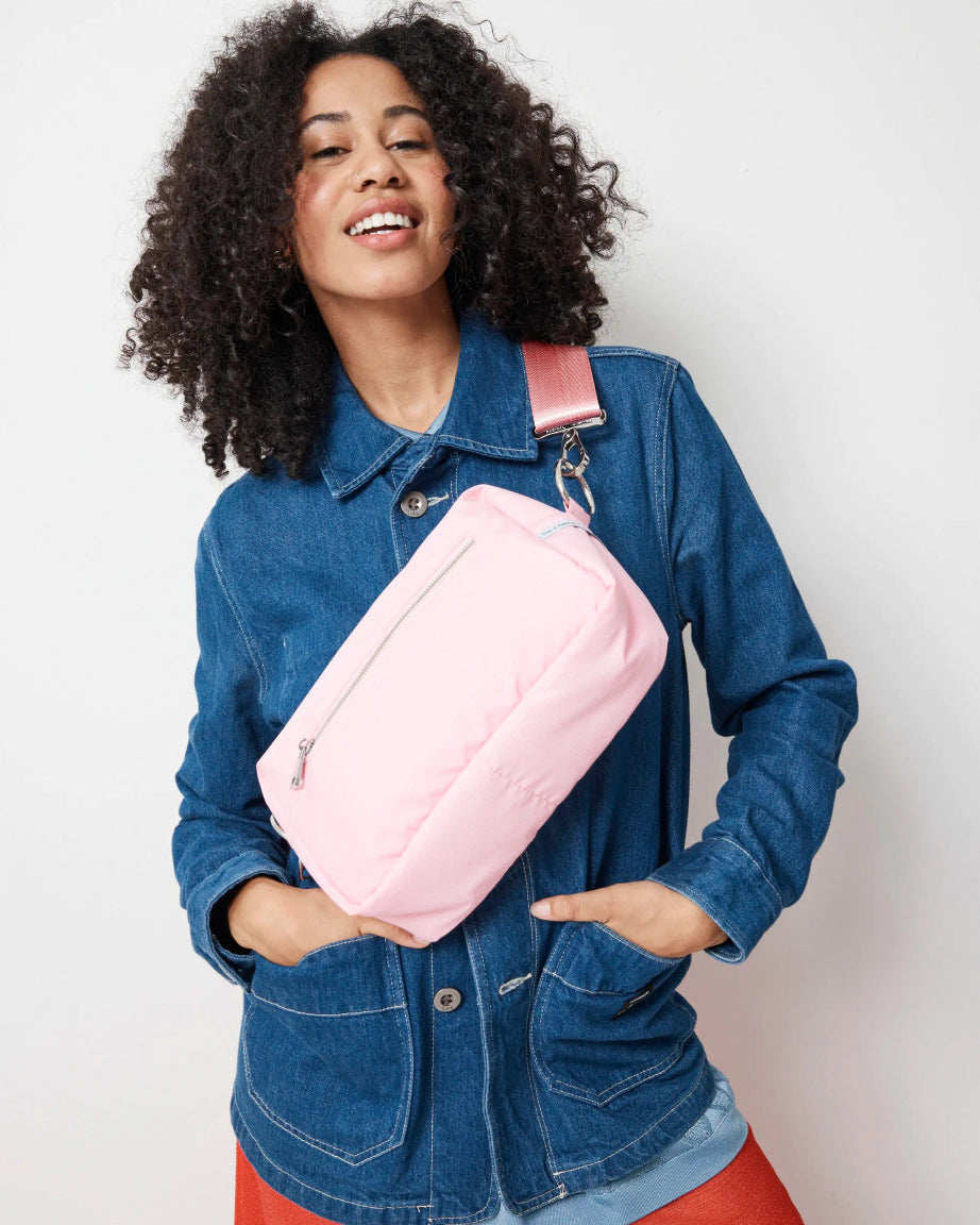 Woman wearing a pink crossbody bag with a plain background